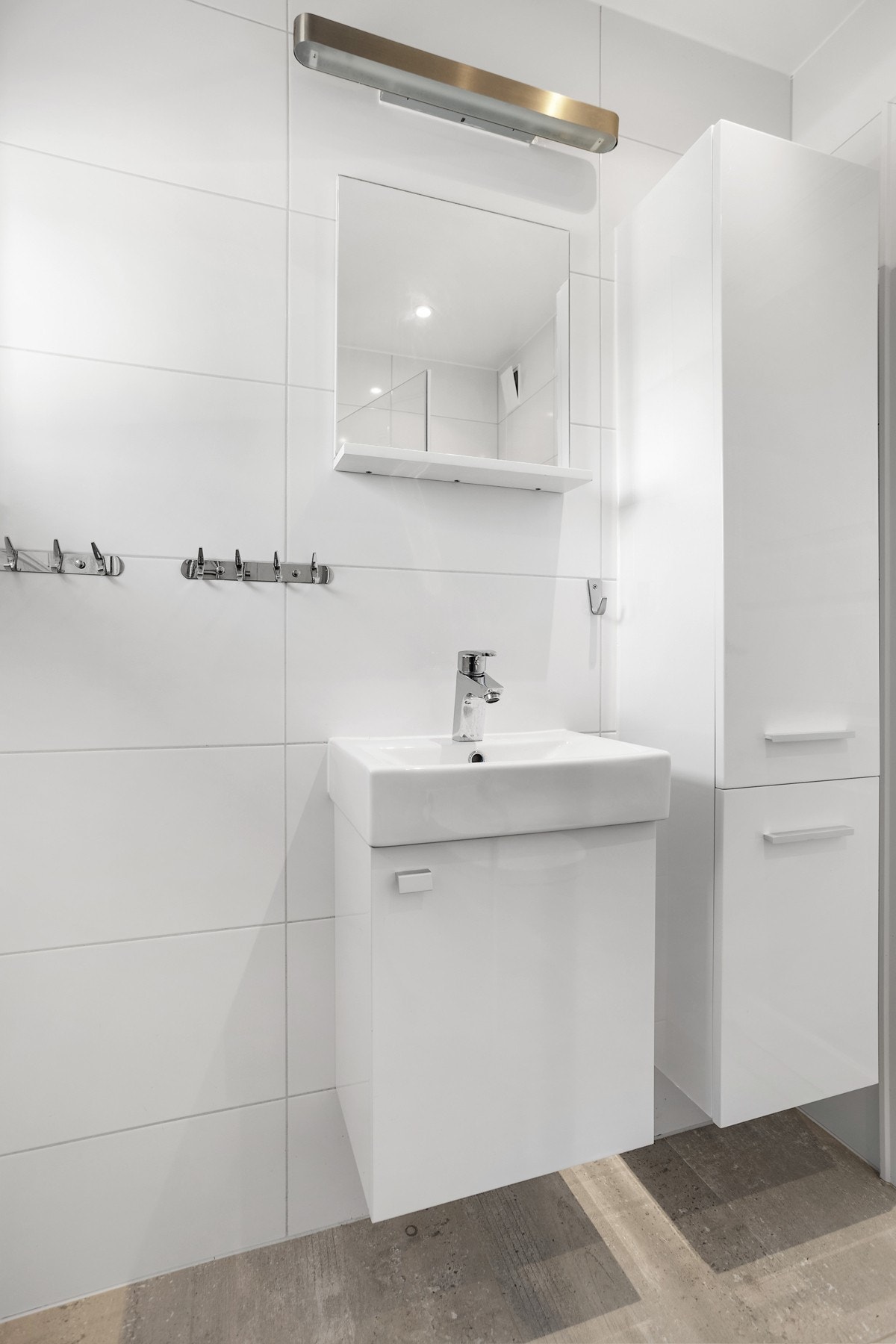 Badet har stilrent servant med underskap, speil med overbelysning og skap Galleribilde