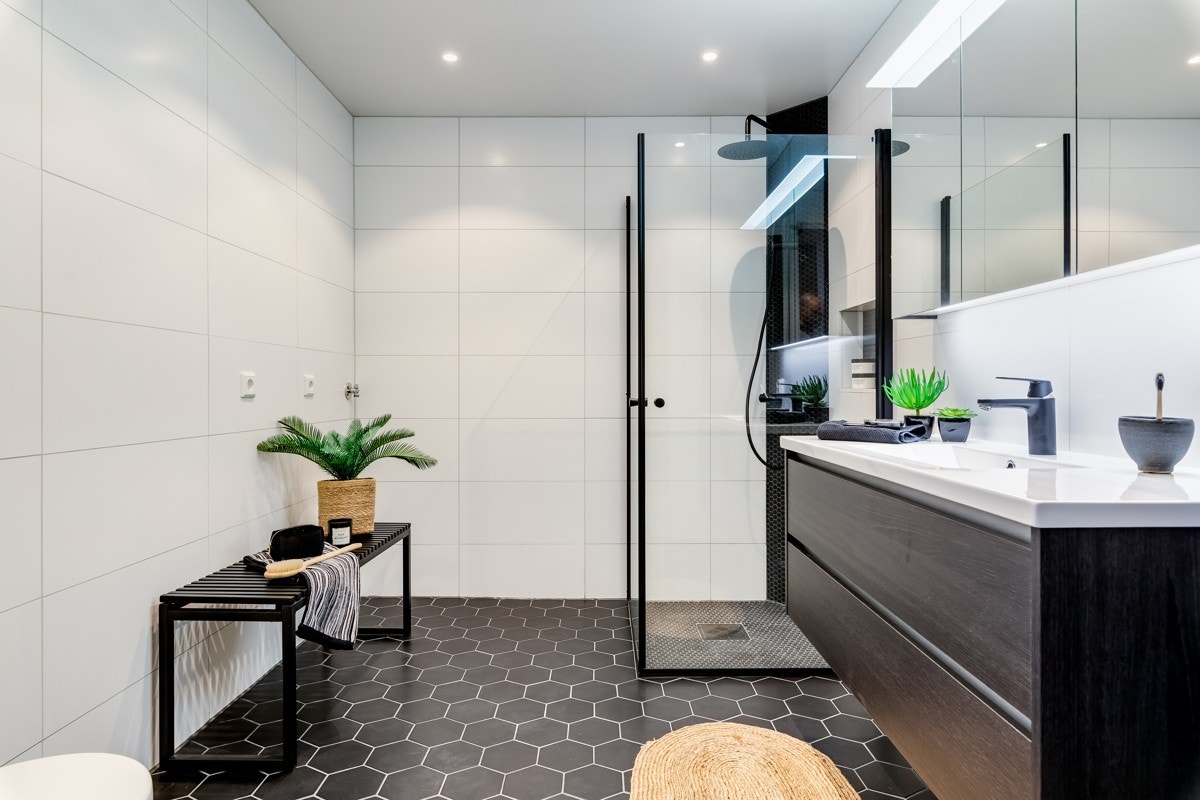 Videre et badet utstyrt med veggmontert toalett og veggskap samt en bred, porselenservant på skuffeseksjon med speilskap og belysning på veggen over. Galleribilde