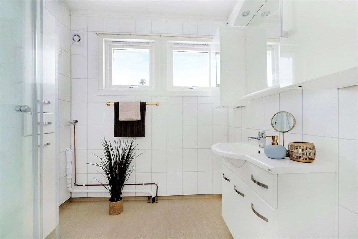 Badet er holdt i en tidløs stil med sandfarget våtromsbelegg, samt hvite flisplater og en stilren baderomsinnredning med heldekkende servant. Galleribilde
