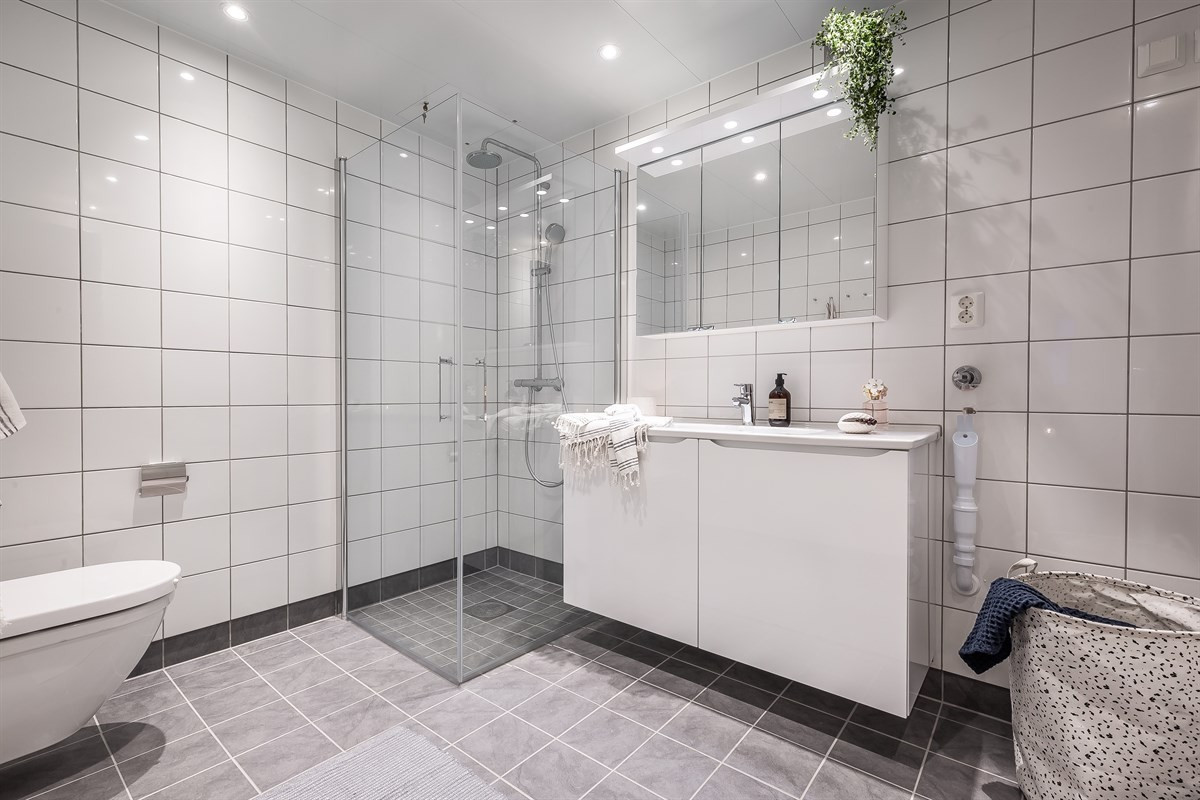 Fliselagt baderom med dusjhjørne, downlights, opplegg for vaskemaskin, og varme i gulv