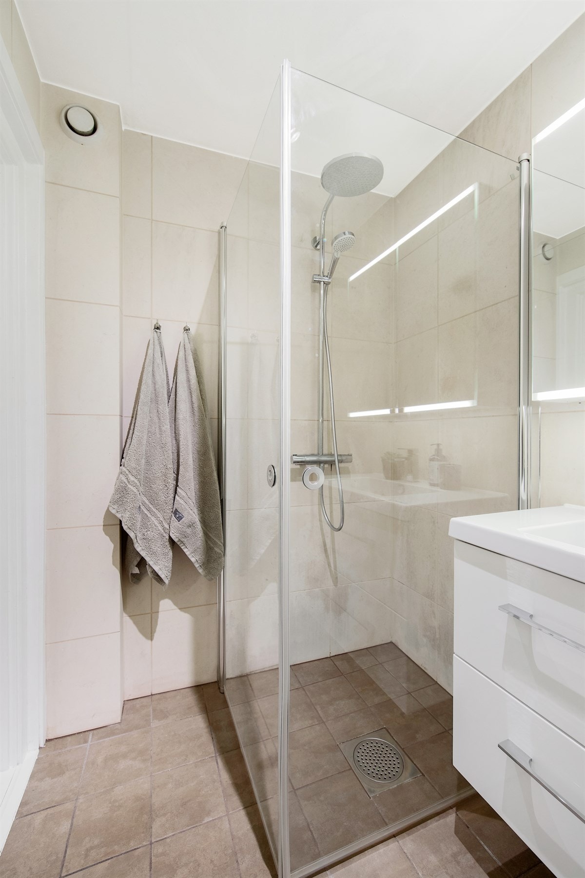 Badet er delikat innredet med gulv- og veggfliser i varme toner, gulvvarme og vegghengt toalett Galleribilde