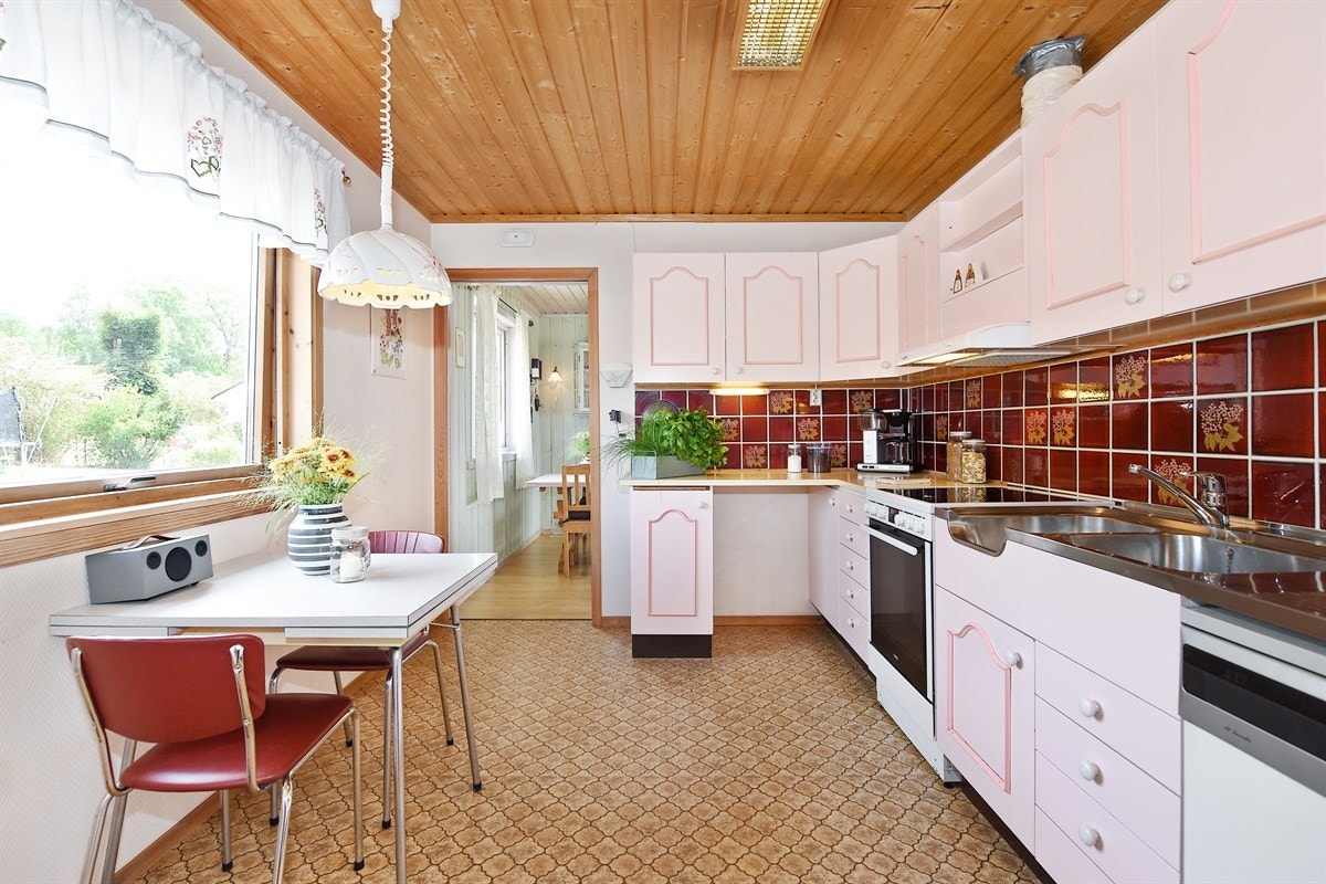 Kjøkkenet har eldre malt kjøkkeninnredning med benkeplate i laminat og stål, fliser mellom over og underskap og frittstående hvitevarer. Galleribilde