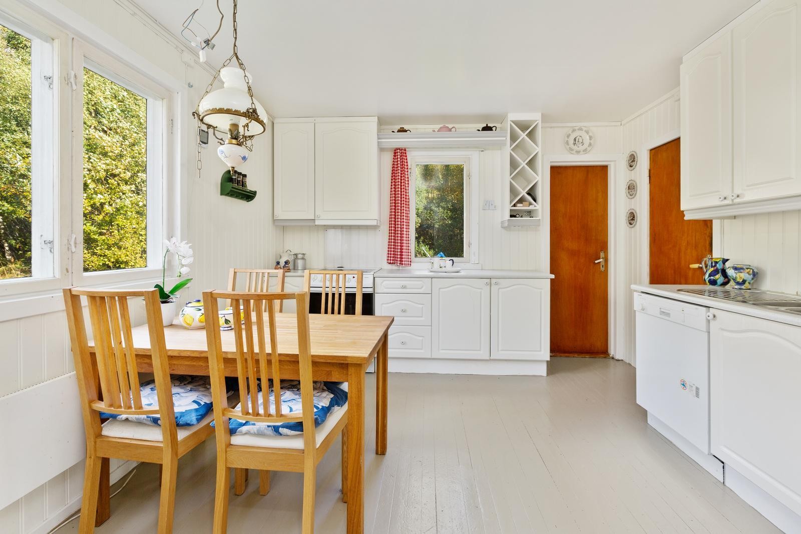 Kjøkkeninnredning med hvite profilerte fronter. Overskap med glass. Mdf-plater over laminert benk og dobbel stålkum. Galleribilde