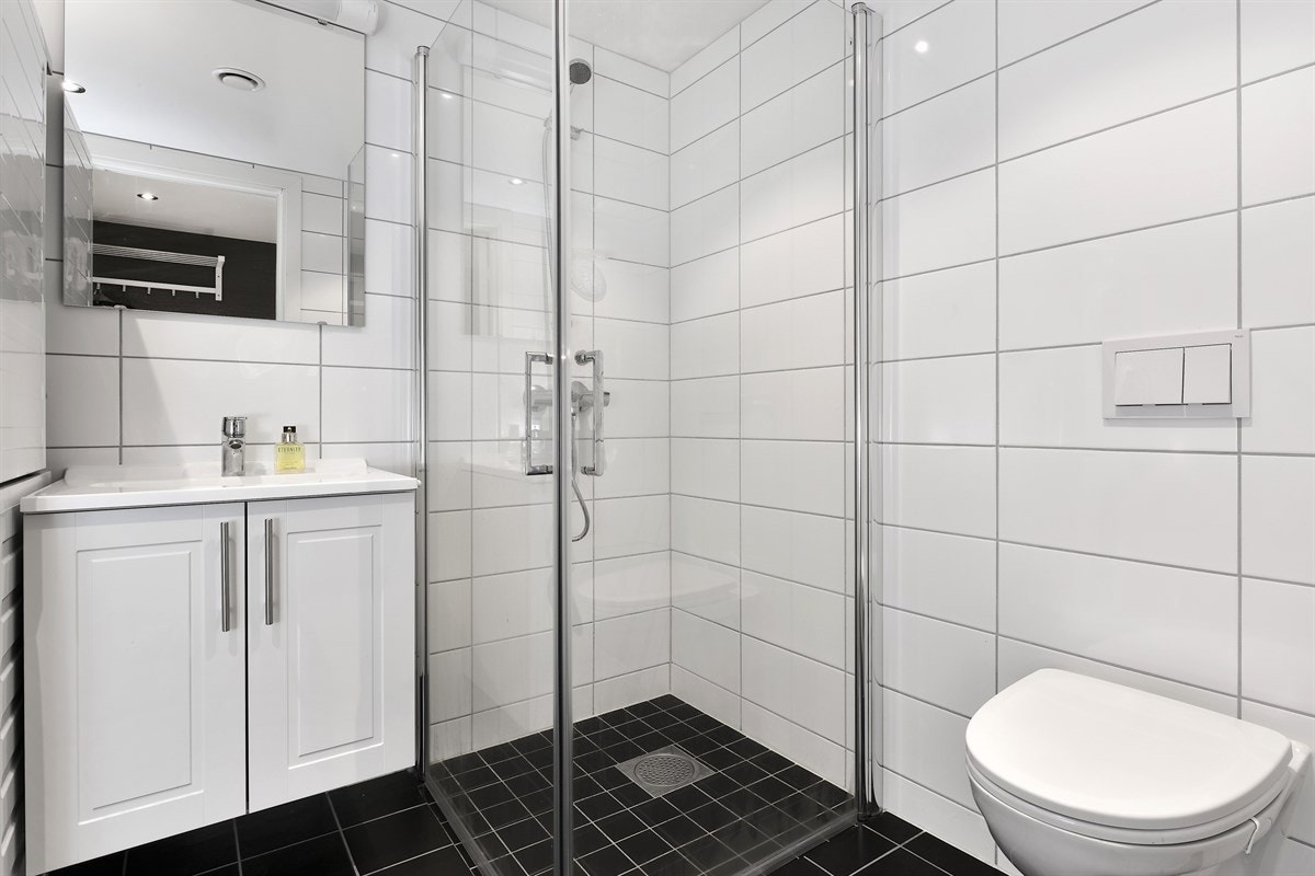 Videre er badet utstyrt med vegghengt toalett og en nedsenket dusjsone med svingbare glassdører. Galleribilde