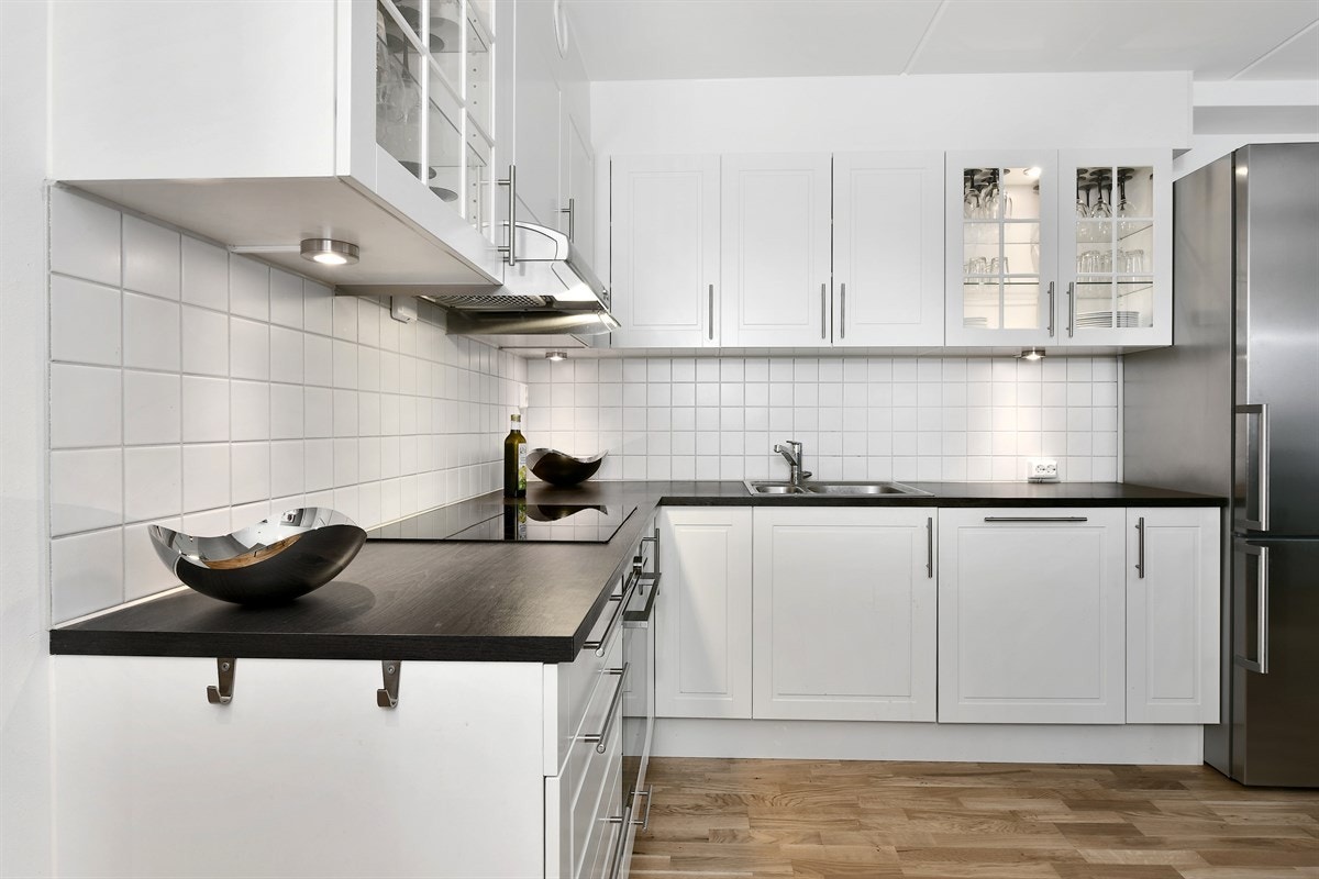 Innredningen har hvite, profilerte fronter, mørk laminatbenkeplate med stålkum og enkelte vitrineskap med integrert belysning. Galleribilde