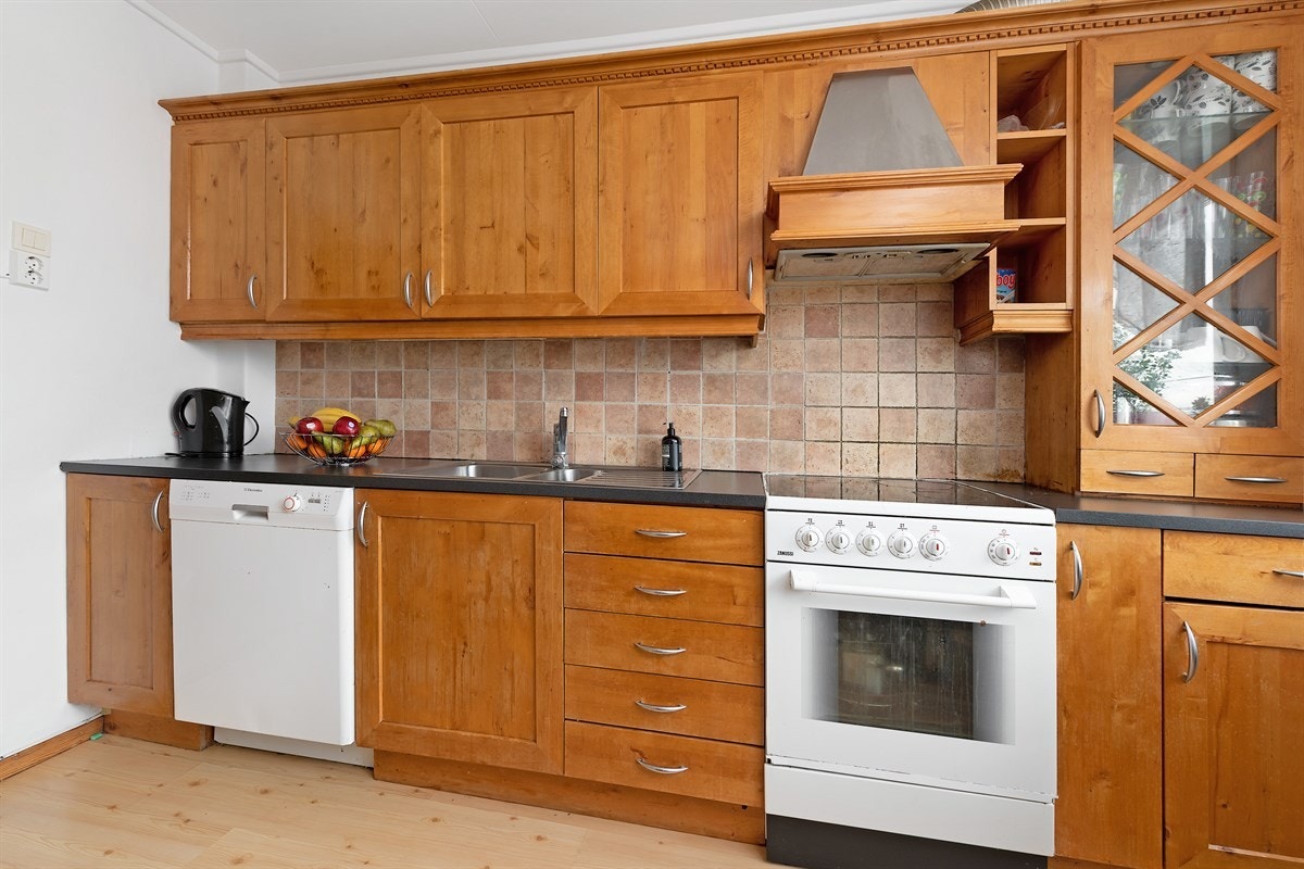 Ventilatorhetten er bygd inn og det er pene, naturfargede fliser over benken. Kjøkkenet har nisje for hvitevarer og opplegg for oppvaskmaskin. Galleribilde