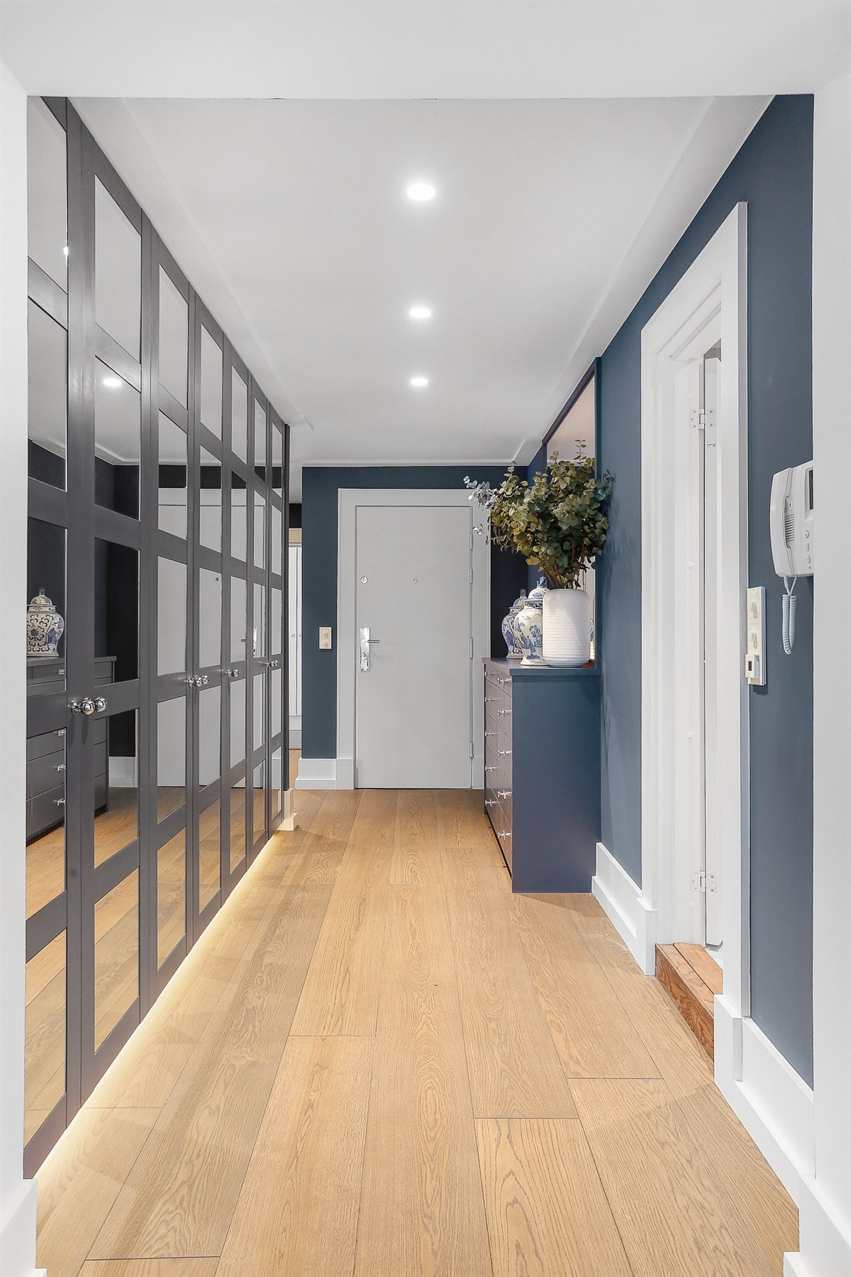 Plassbygd skapinnredning i gang/entré. Skapene har fronter med speil og rammer og fyller omtrent hele den ene langveggen. Galleribilde