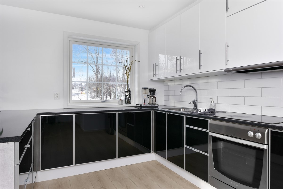 Videre har innredningen mørk laminatbenkeplate med dobbel oppvaskkum i stål, lyse metrofliser over benken, spiseplass ved barløsningen og downlights. Galleribilde