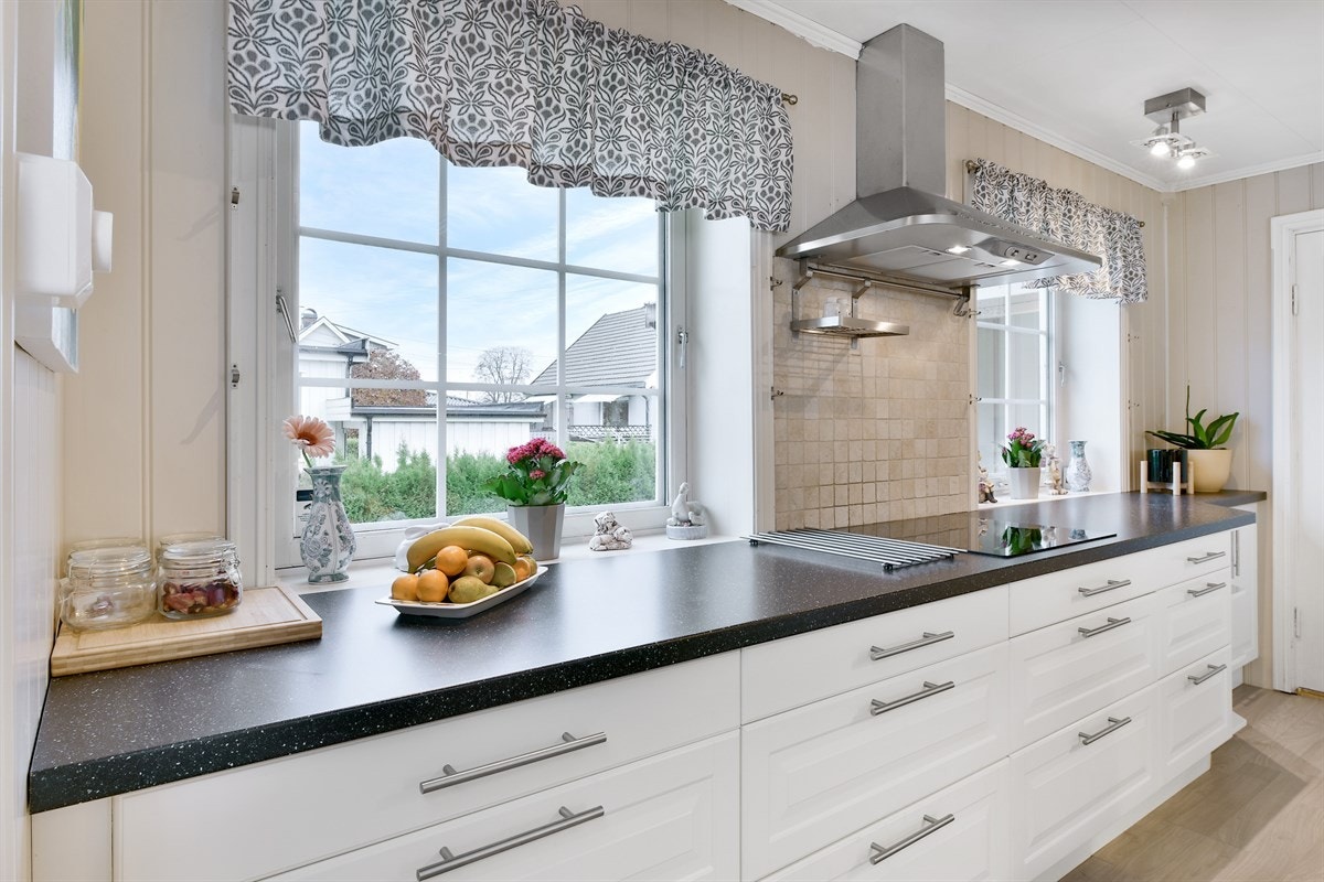 Frontene er i lys, profilert utførelse, flere steder med vitrineglass, og benkeplaten er i sort laminat med nedfelt stålkum. Galleribilde