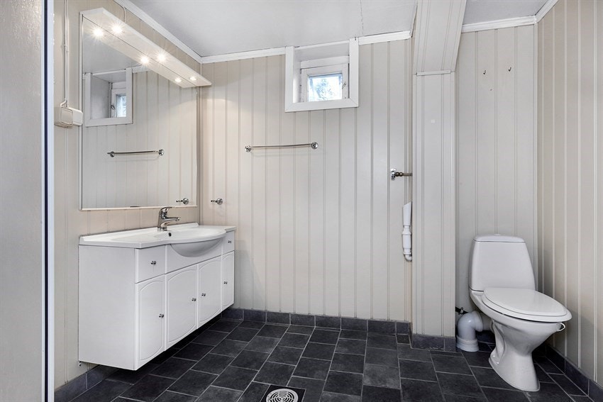 Rommet har speil med overbelysning, servantmøblement med profilerte fronter, frittstående toalett og dusjkabinett. Det er også opplegg for vaskemaskin på dette badet. Galleribilde