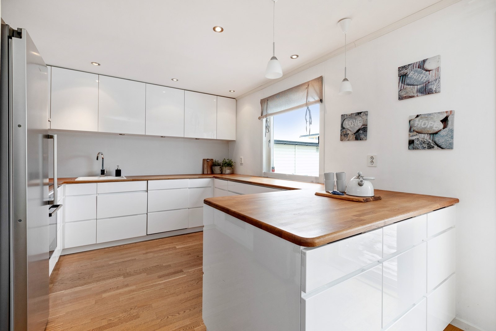 Nyere kjøkkeninnredning fra 2010 med hvite høyglansfronter og heltre benkeplater Galleribilde