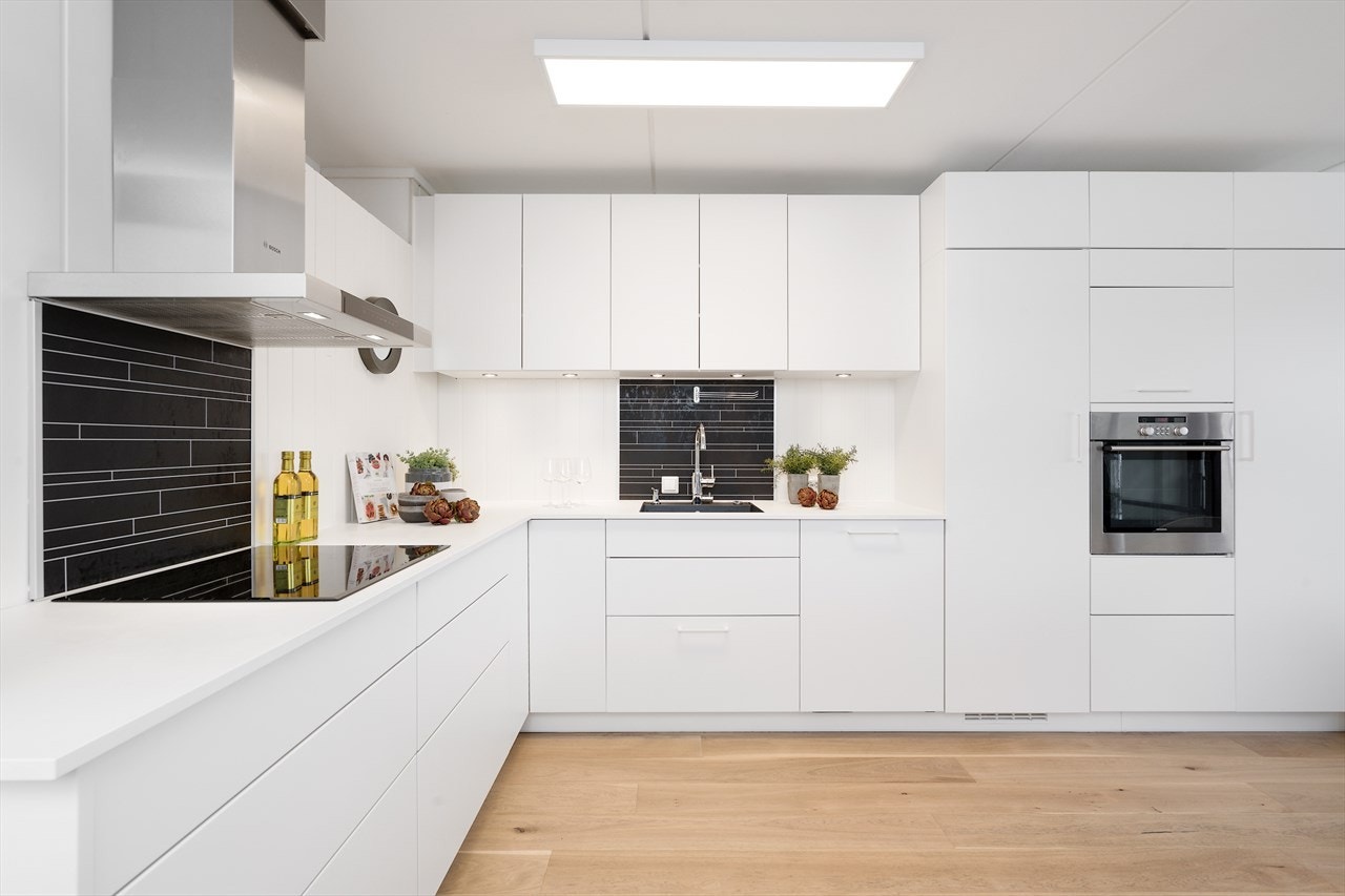 Lyst og lekker kjøkkeninnredning med rikeglig av skap- og benkeplass. Kjøkkeninnredning fra Kvik (2016) Innredningen er med glatte fronter i matt hvit utførelse, benkeplate i laminat og underlimt oppvaskkum i rustfritt stål. Galleribilde