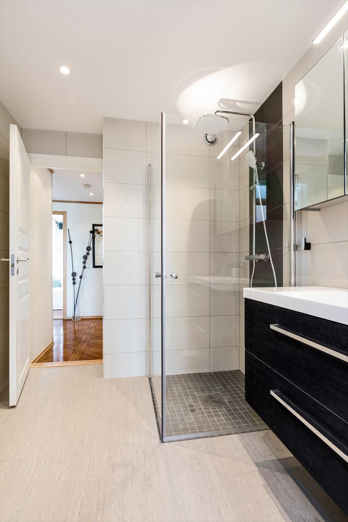 Flislagt baderom med varme i gulv. Innredning fremstår med dusjplass med veggmonterte glassdører og servant med underskap Galleribilde