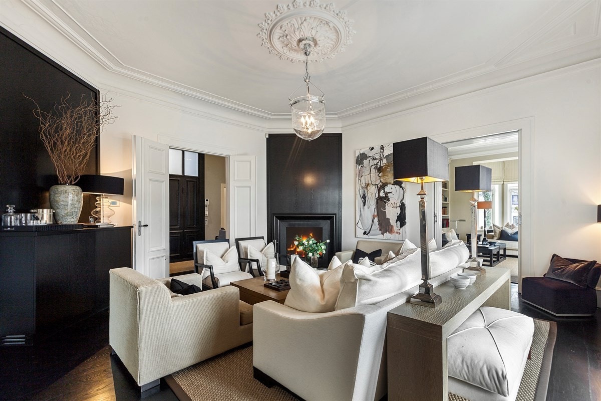 Peisestuen ar en tofløyet terrassedør i glass. Utenfor er det en solrik terrasse og adkomst til den private hagen. Peisen er satt i et hjørne, og er innebygd i et sort trepanel. Galleribilde