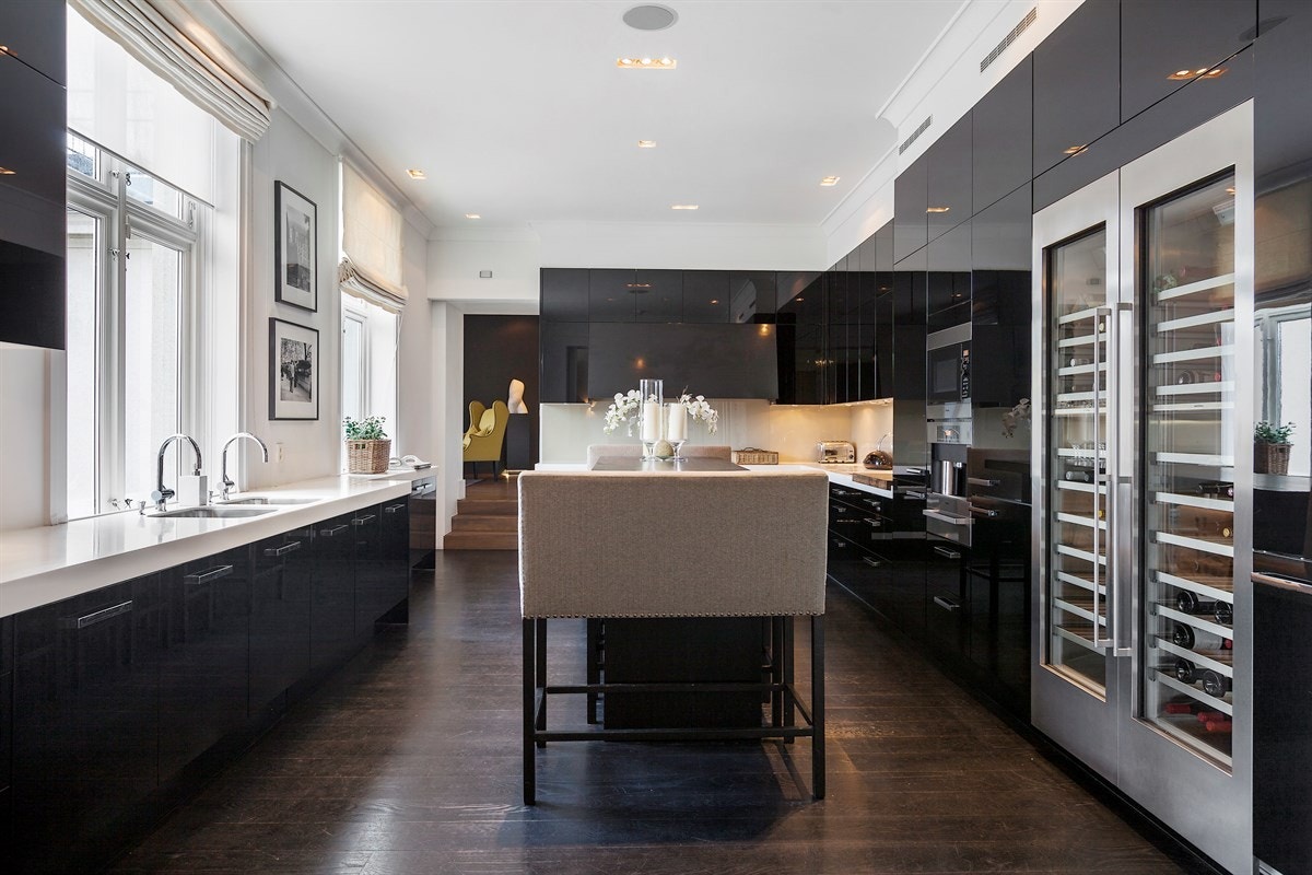 Praktfullt hovedkjøkken med eksklusiv, takhøy innredning fra Poggenpohl i sort høyglans. Benkeplaten er i vakker hvit Corian med tre underlimte oppvaskkummer og tre armaturer. Galleribilde