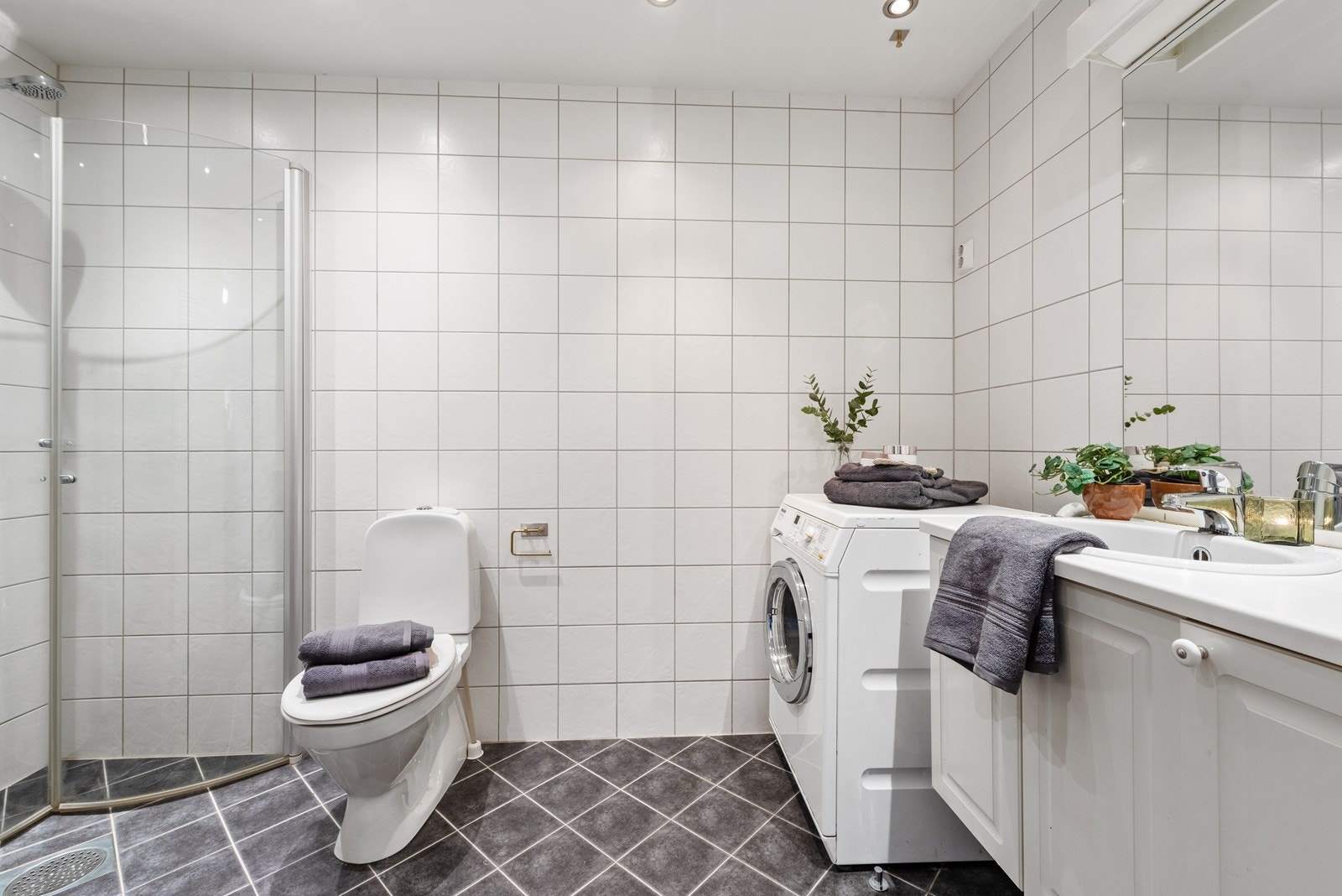 Romslig bad med dusjhjørne, toalett, servant med underskap og opplegg for vaskesøyle. Galleribilde