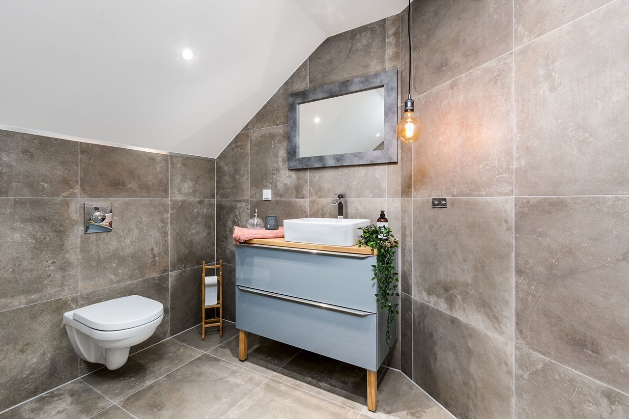 Badet har lekre, flissatte overflater i dempede jordfarger, og fine detaljer som downlights, gulvvarme og nisje til såper i dusjhjørnet. Galleribilde