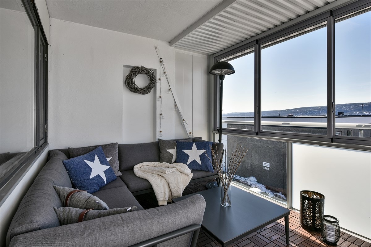 Balkongen har nyere trelemmer på gulvet, hvitmalte vegger og rekkverk i metall og glass. Galleribilde