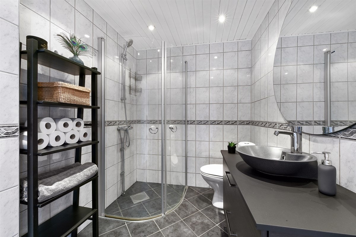 Badet i leiligheten har lyse fliser på veggene, downlights i himling og mørkgrå fliser på gulv med gulvvarme. Galleribilde