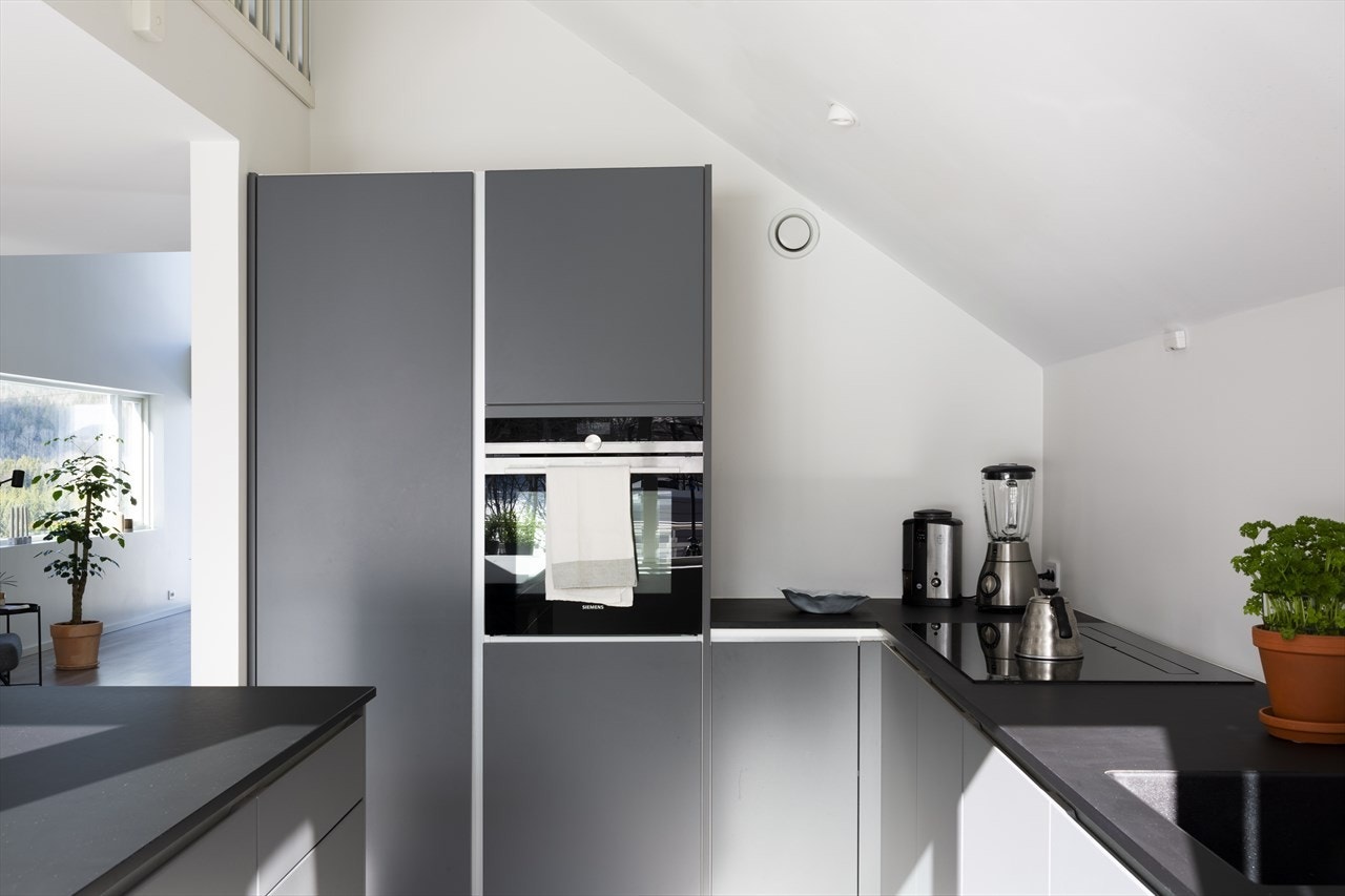 Kjøkkenet er moderne og lekkert, med pent laminatgulv, downlights, hvitmalte overflater og store vinduer. Galleribilde