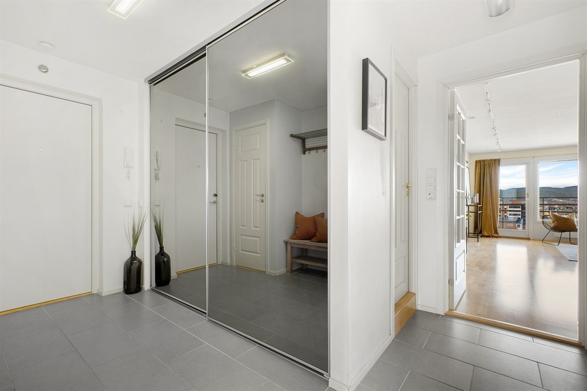 Leiligheten har en romslig entré med fliser i gulv med behagelig gulvvarme og stor skyvedørsgarderobe med speilfront for god oppbevaringsplass. Galleribilde