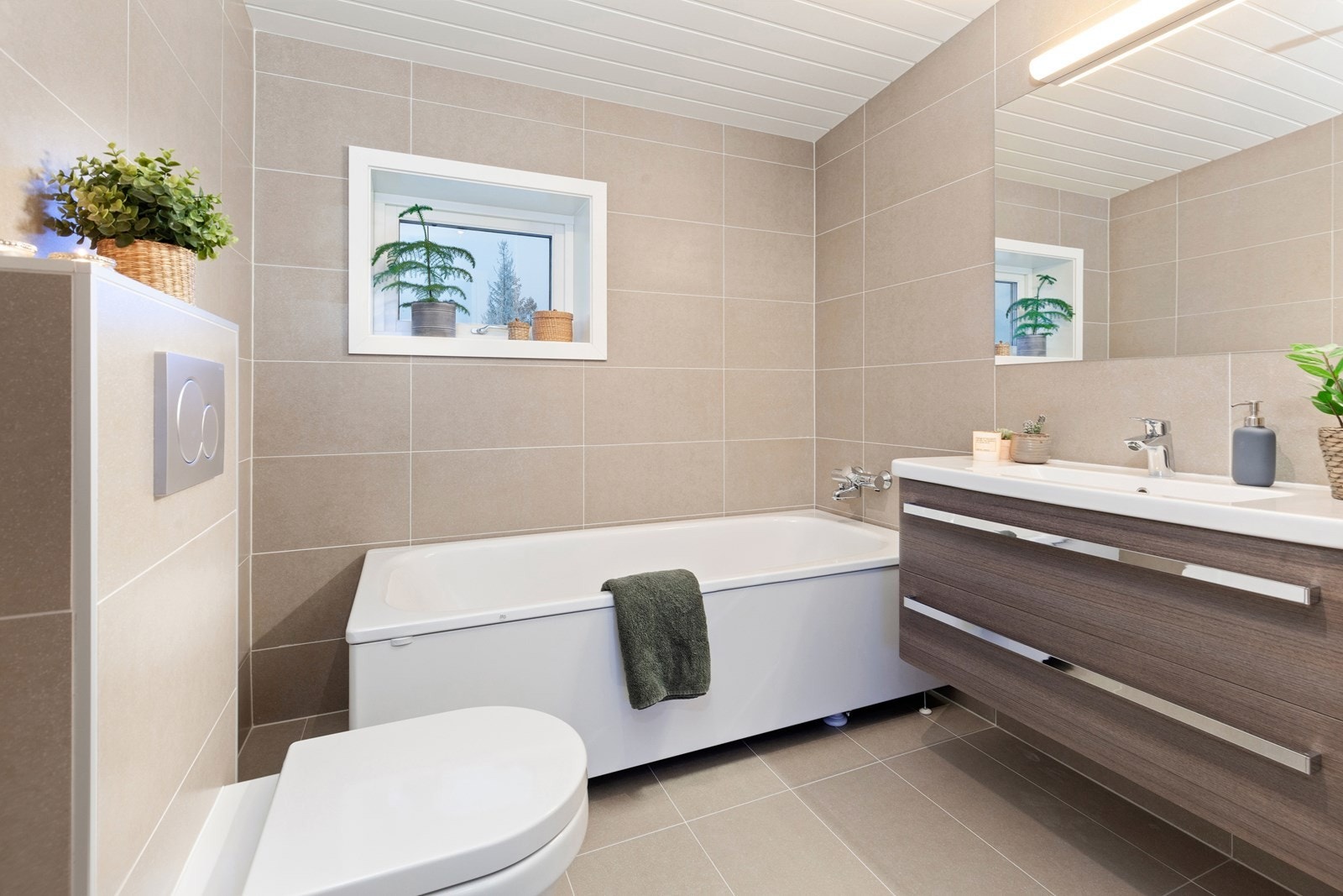 Badet har store fliser på gulv og på vegger, gulvvarme, downlights og et veggmontert toalett. Galleribilde