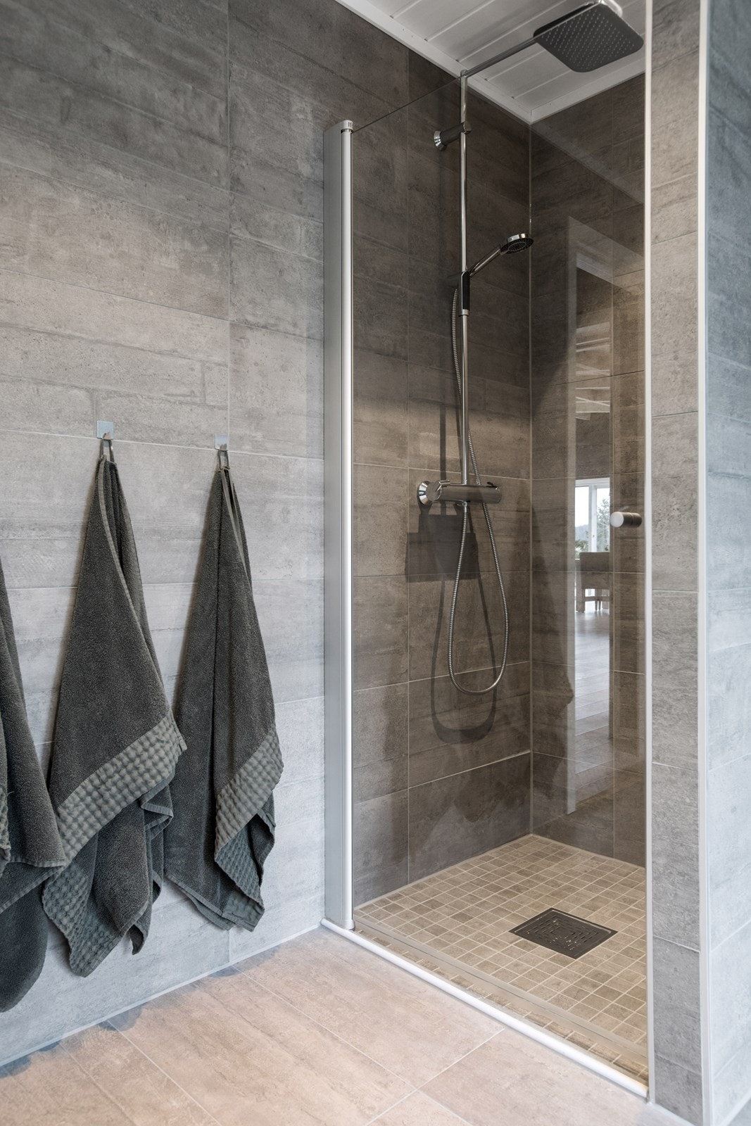 Det andre badet i første etasje har grå fliser på gulv og deler av vegger, dels malte vegger, gulvvarme, downlights og et veggmontert toalett. Galleribilde