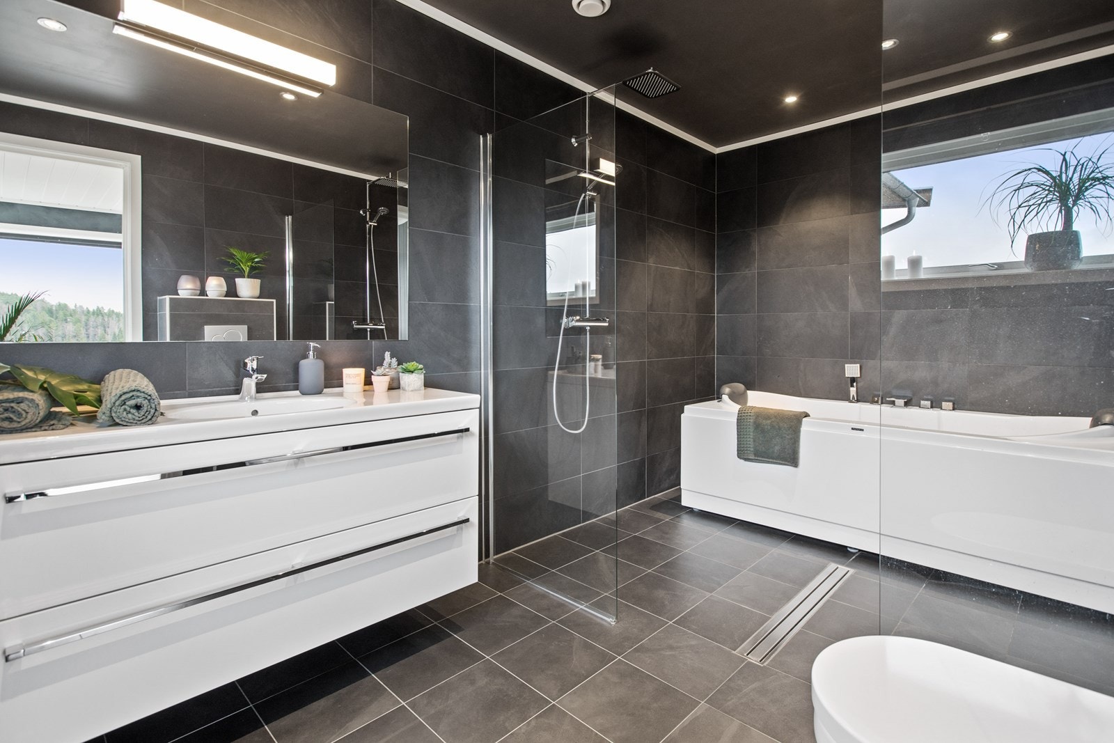 Resten av badet er også flislagt, og rommet har lun gulvvarme, veggmontert toalett og en heldekkende servant med underskuffer. Over servanten er det montert speil med belysning. Galleribilde