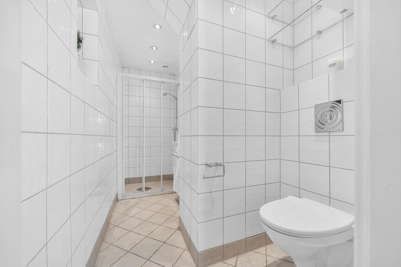 Flisalgt bad med vegghengt toalett, servant med skap og dusjhjørne. Galleribilde