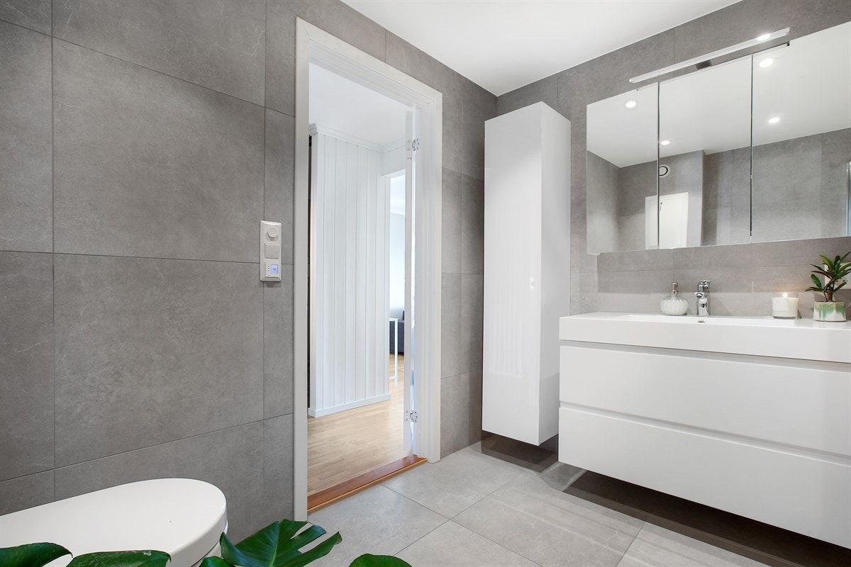 Badet består av åpen dusjplass med slagdører og dusjgarnityr med takdusj, heldekkende servant i skapinnredning, speilskap, høyskap, vegghengt toalett. Det er også opplegg for vaskemaskin. Galleribilde