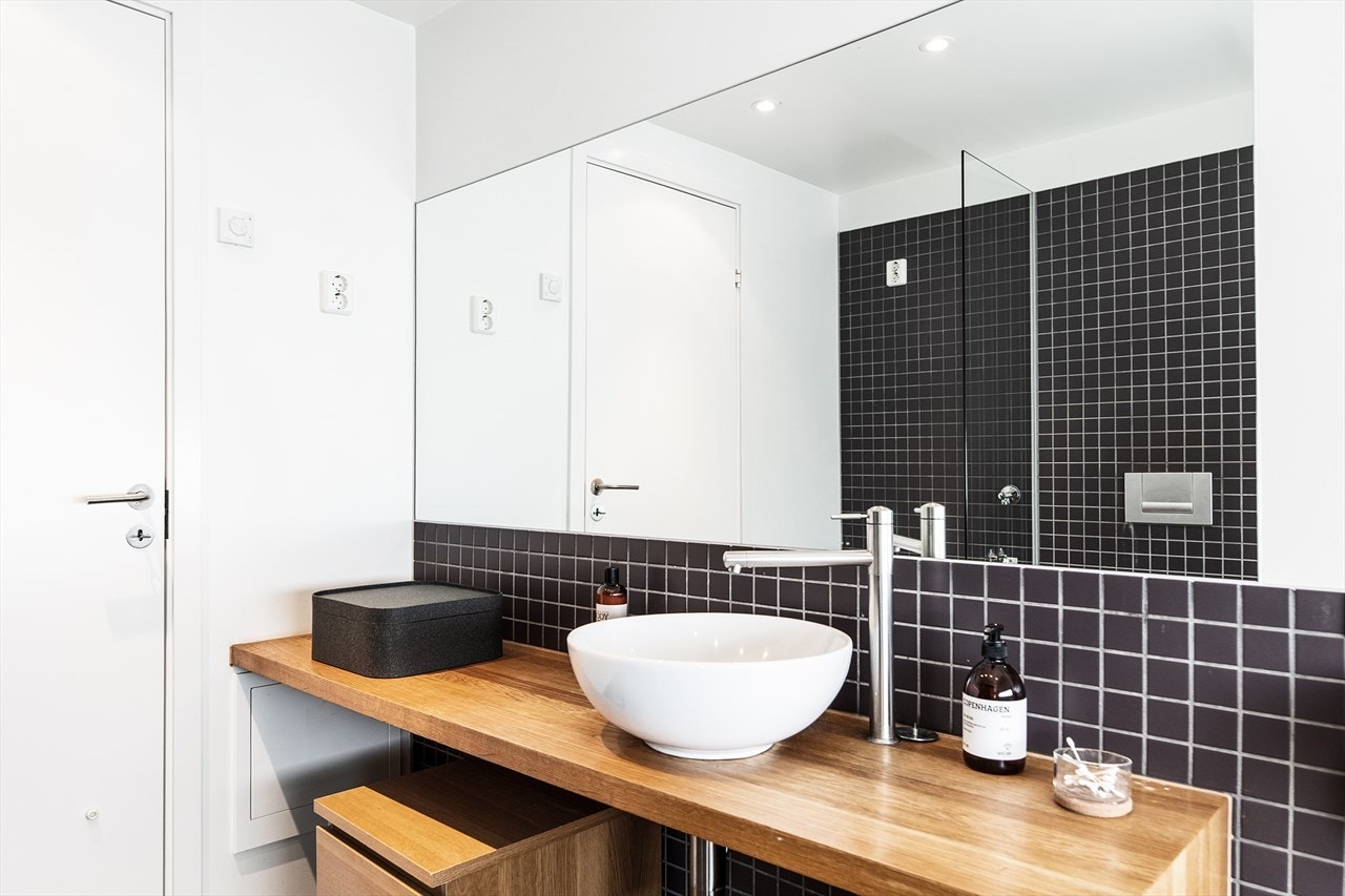 Pent bad med heltre benkeplate og fine kontraster med mørke fliser og lyse flater. Galleribilde