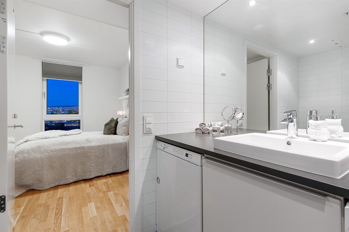 Det romslige badet har en lun og delikat fargepalett med fliser i en gråtone på gulv og hvite fliser på vegg Galleribilde