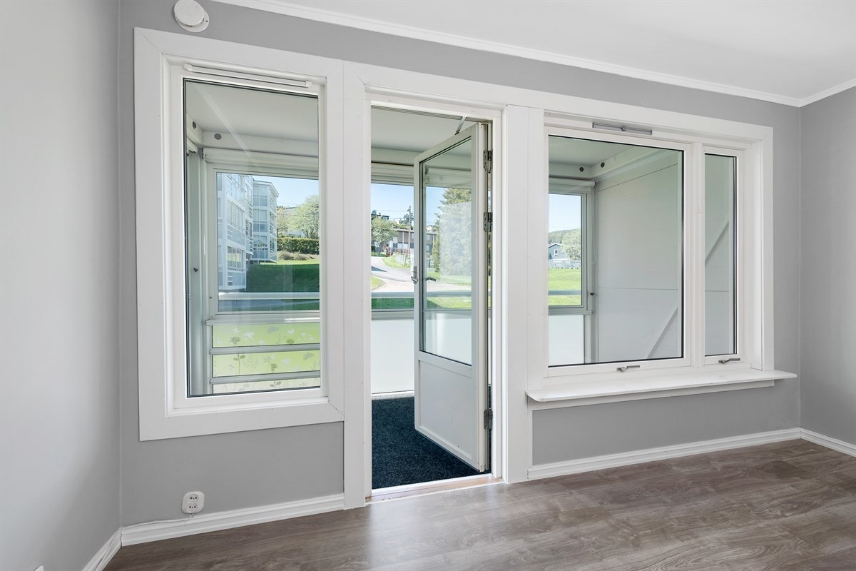 Leiligheten har en luftig stue med vinduer og glassdør som vender mot en innglasset balkong. Galleribilde