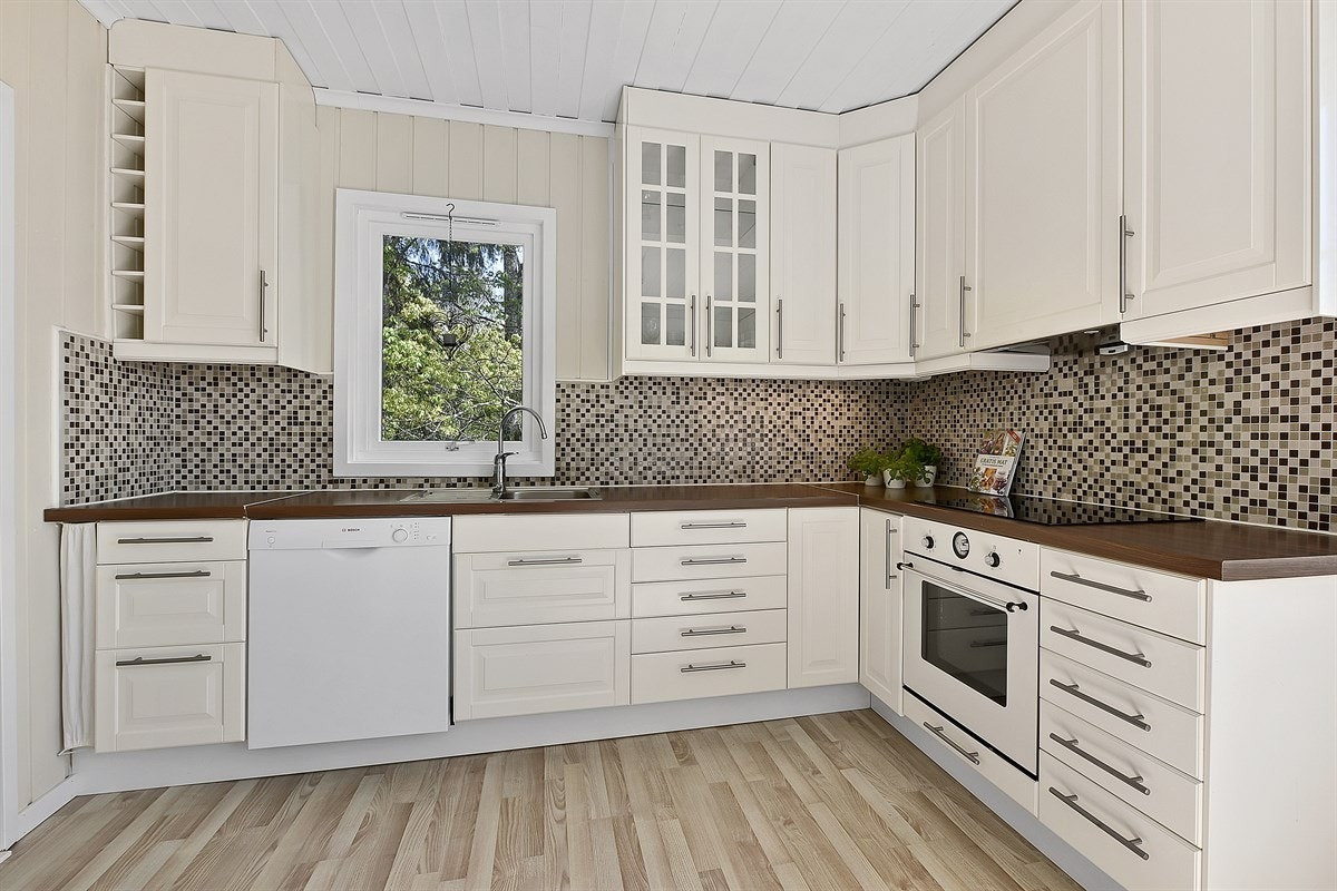 Et herlig, lyst kjøkken ligger i eget rom, med laminatgulv og lysmalte panelvegger. Galleribilde