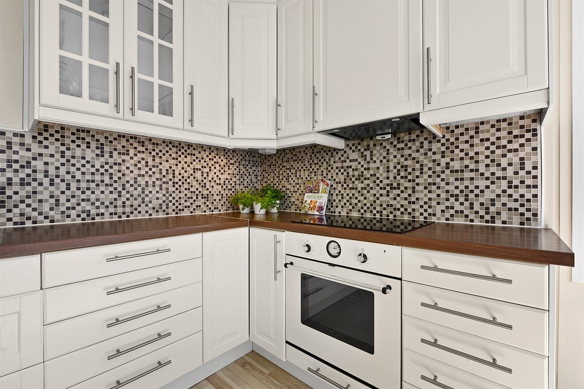 Over benken er det belysning og mørke mosaikkfliser, og over kokesonen er det montert en ventilator. Galleribilde