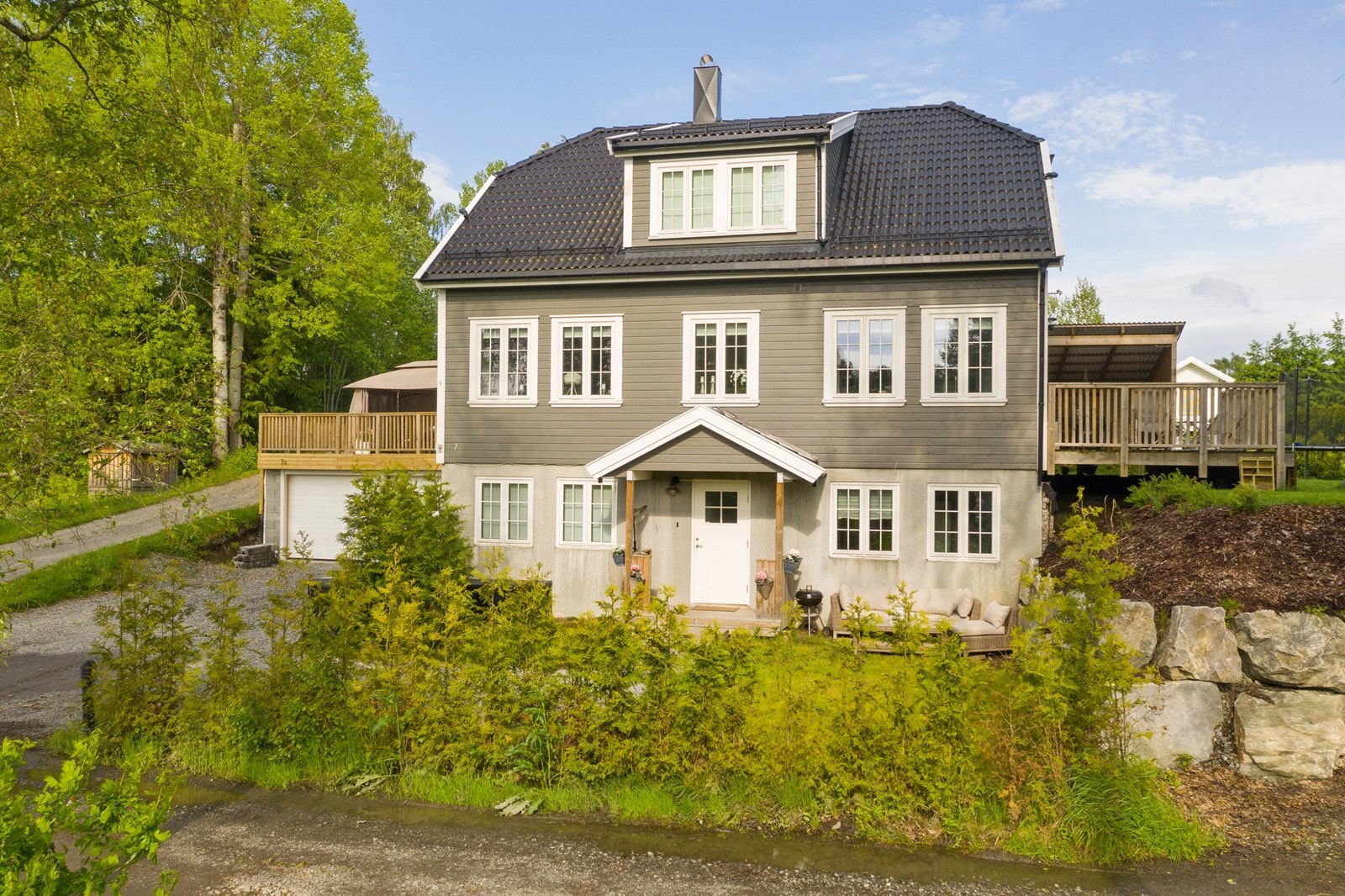 Tomten er pent opparbeidet over to nivå med plen, prydbusker og støttemurer Galleribilde