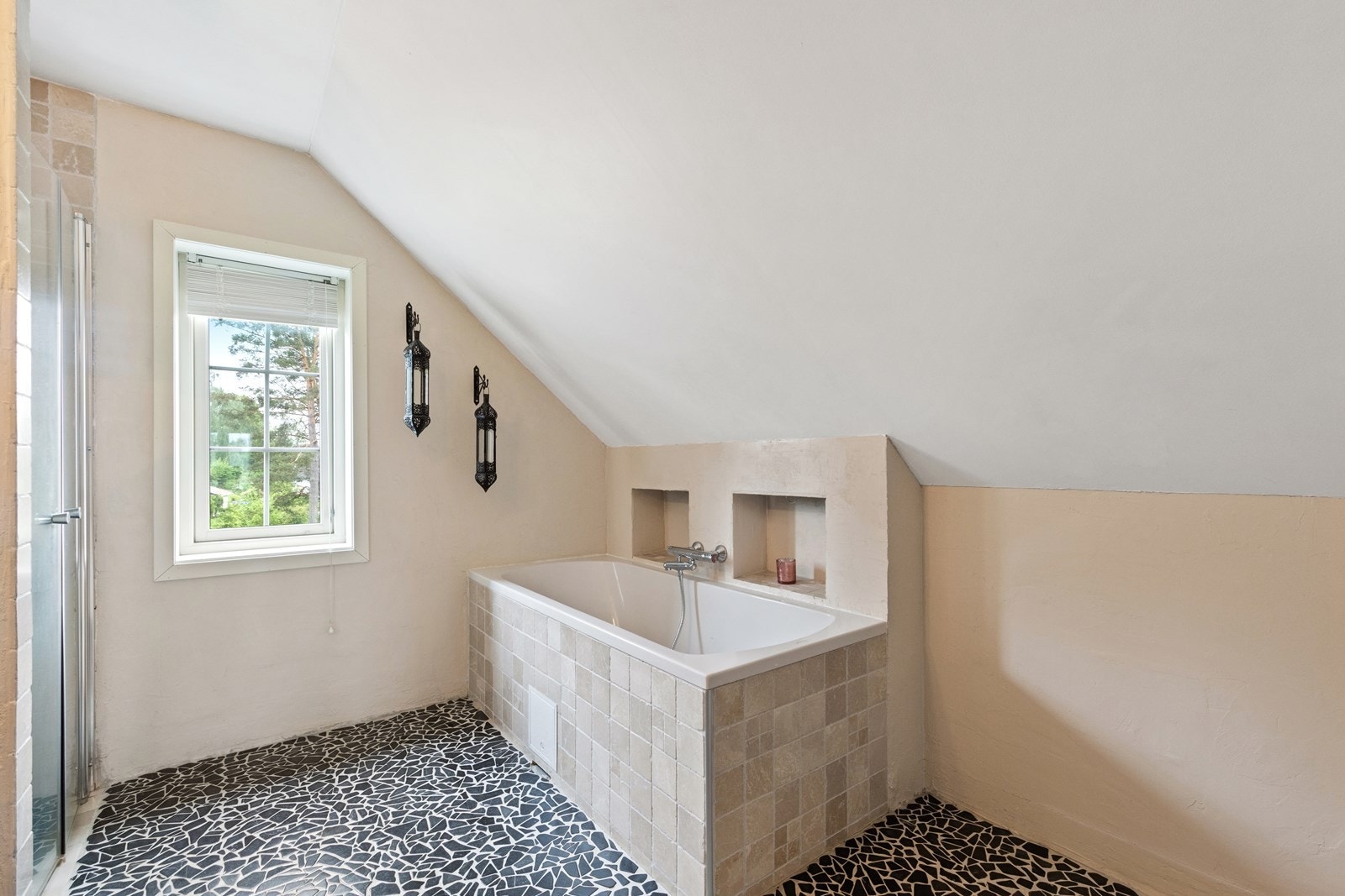 Det er utstyrt med et innmurt badekar, vegghengt toalett og dusjnisje med glassdører. Galleribilde