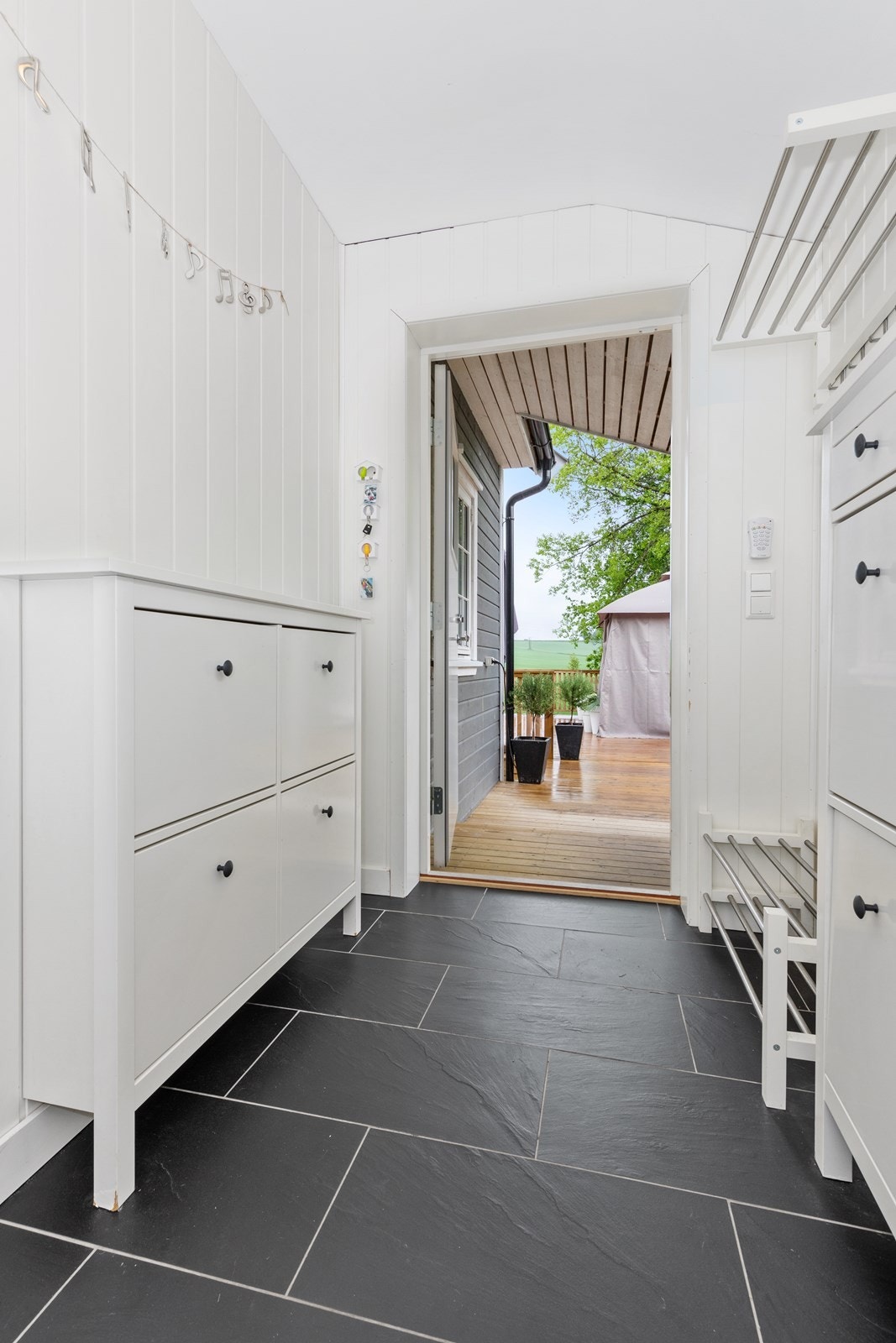Entreen har hvitmalte panelvegger og grå fliser på gulv Galleribilde