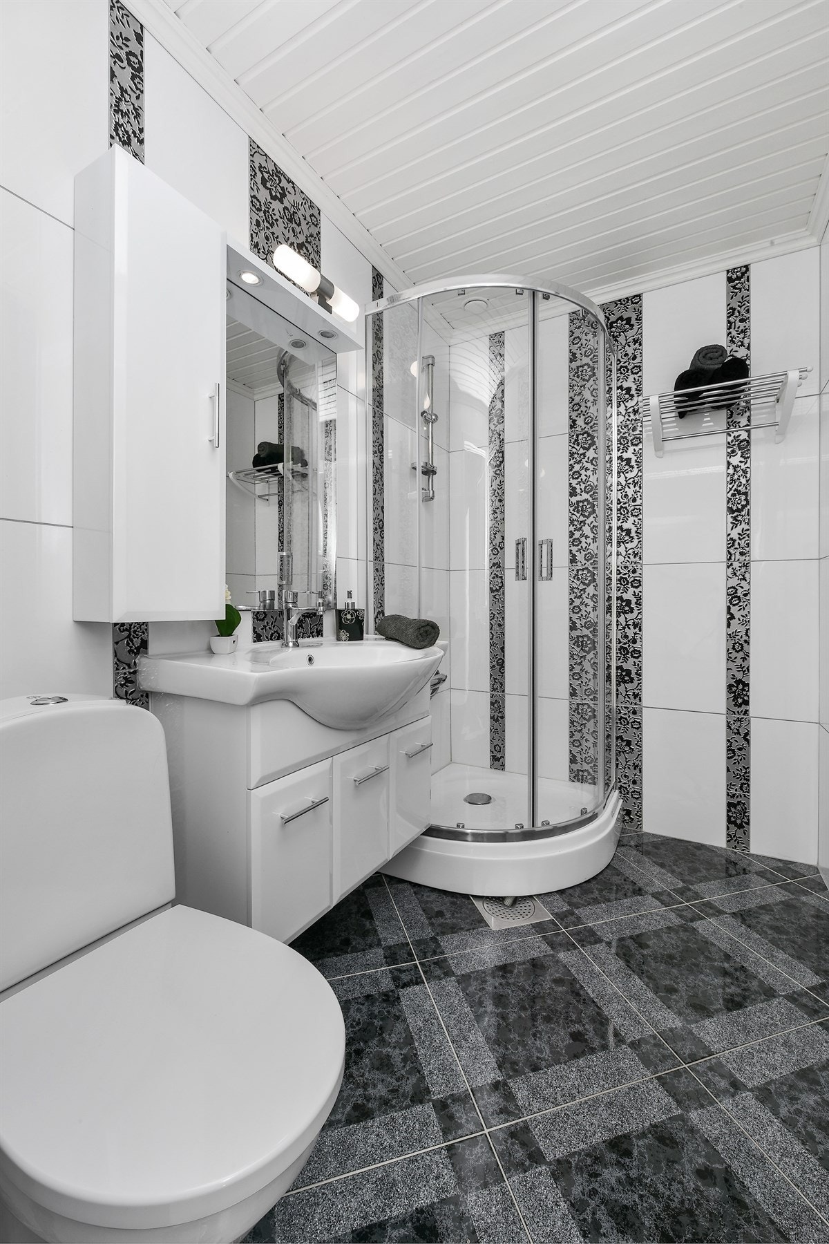 Badet har flislagte flater i grått og hvitt, gulvvarme og toalett. Galleribilde