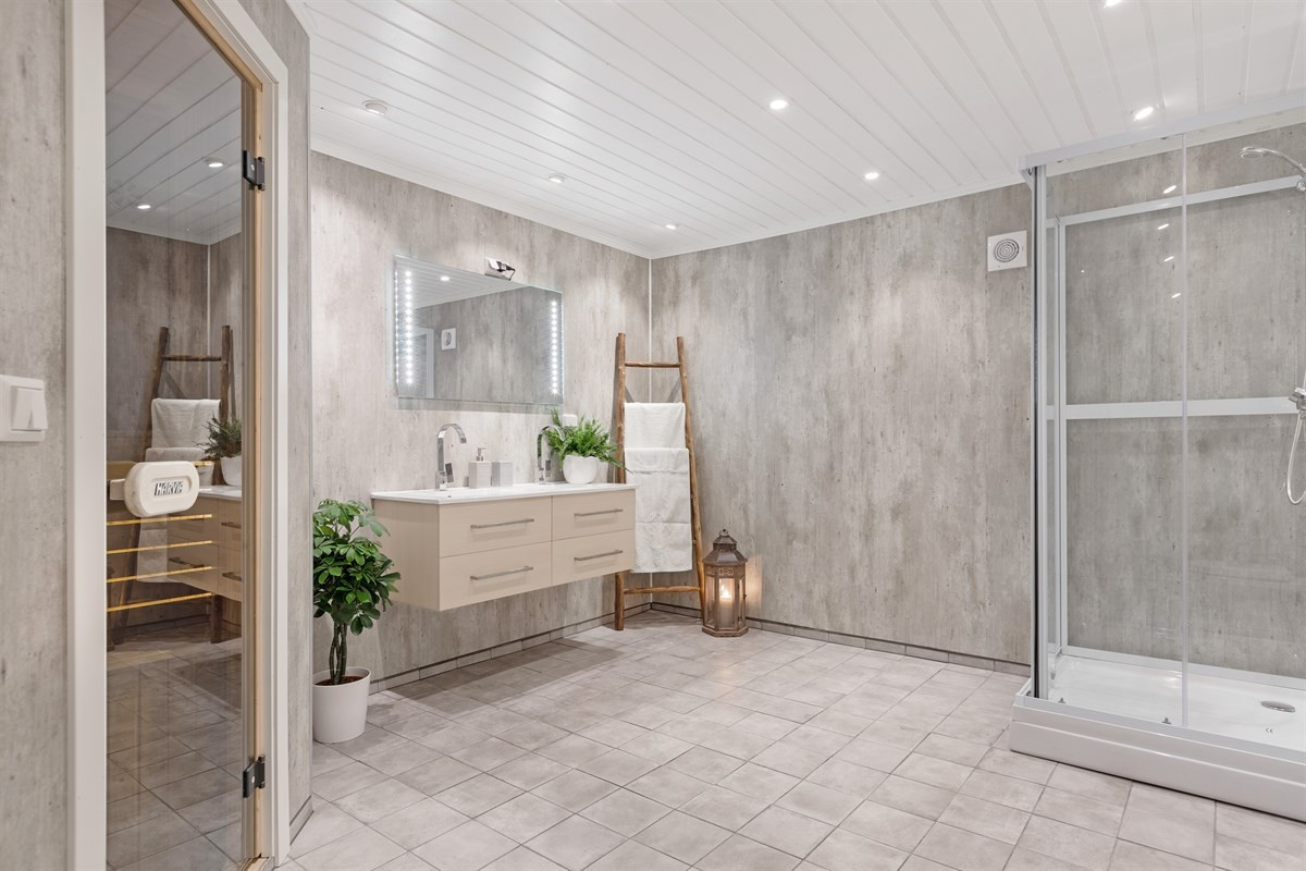 Bad i 0. etasje er innredet med fliselagt gulv, doble servanter, vegghengt wc, downlights, varmekabler i gulv, dusjkabinett samt badstu