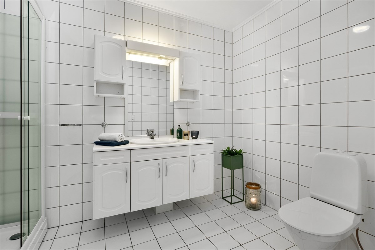 Badet er utstyrt med enkel servant nedfelt i hvit servantskap, to veggskap, speilbelysning, toalett og dusjkabinett. Galleribilde