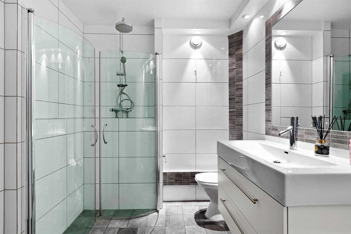 Badet består av servant i skapinnredning, innfliset speil, høyskap, toalett og åpen dusjplass med slagdører. Galleribilde