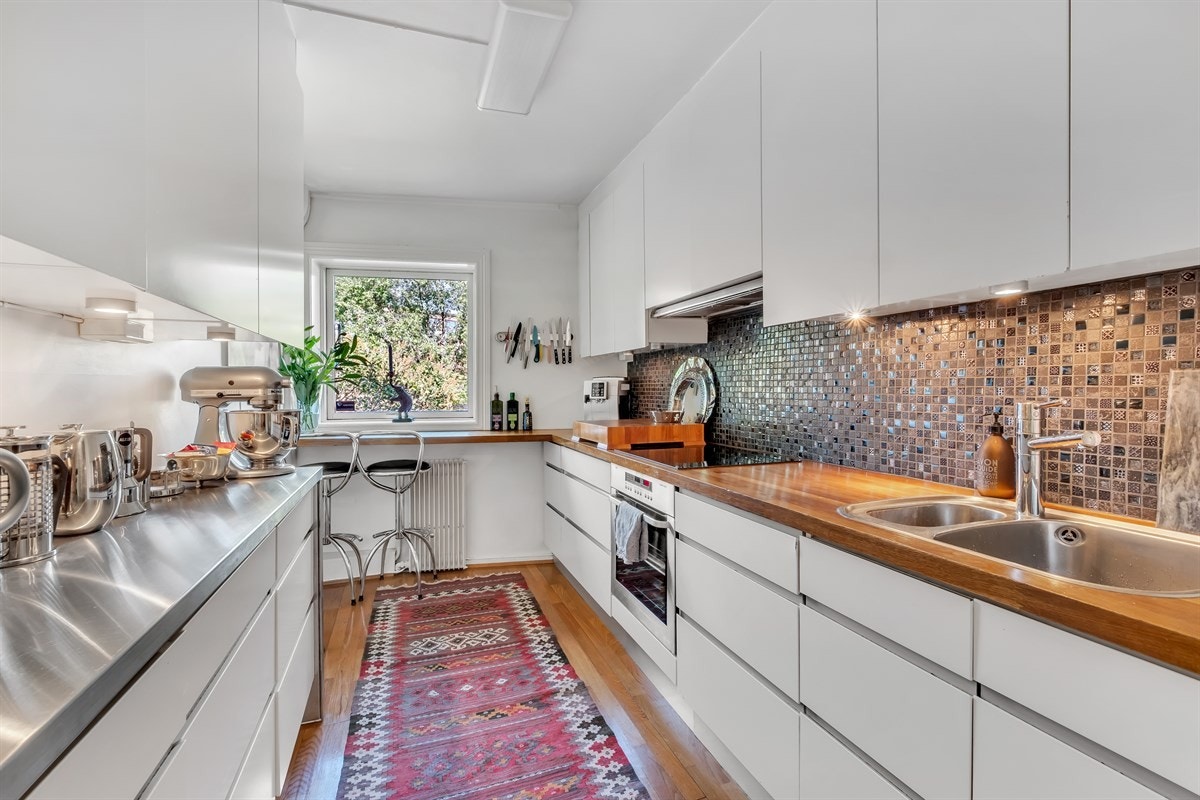 Kjøkken med innredning fra 2005 som består av glatte fronter med integrerte håndtak, to stålkummer med blandebatteri, heltre og stål benkeplater Galleribilde