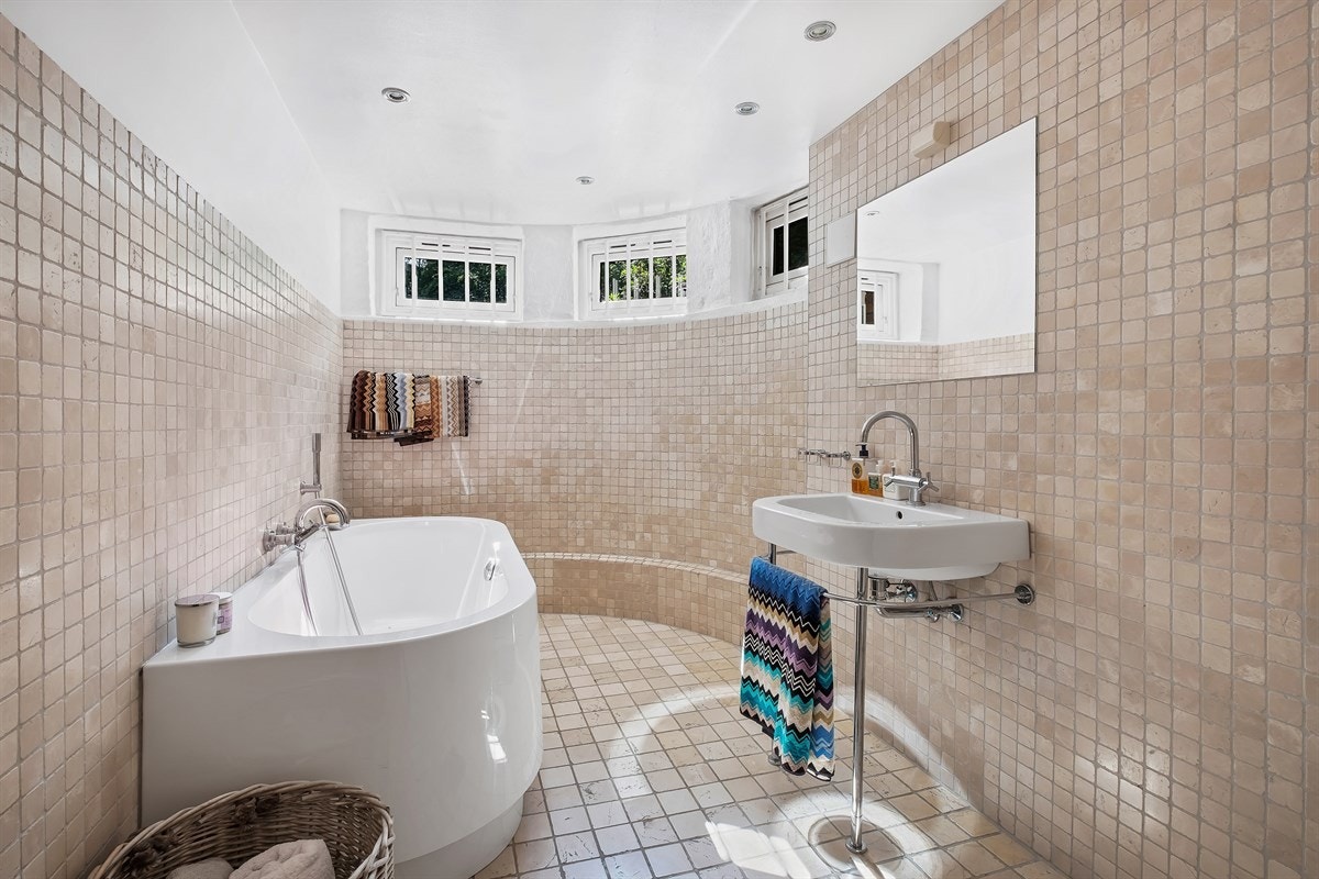 Baderom i 1. etg. med varmekabler i gulv. Frittstående badekar, servant med blandebatteri på søyler, rør skjult i vegg, åpent dusjhjørne Galleribilde