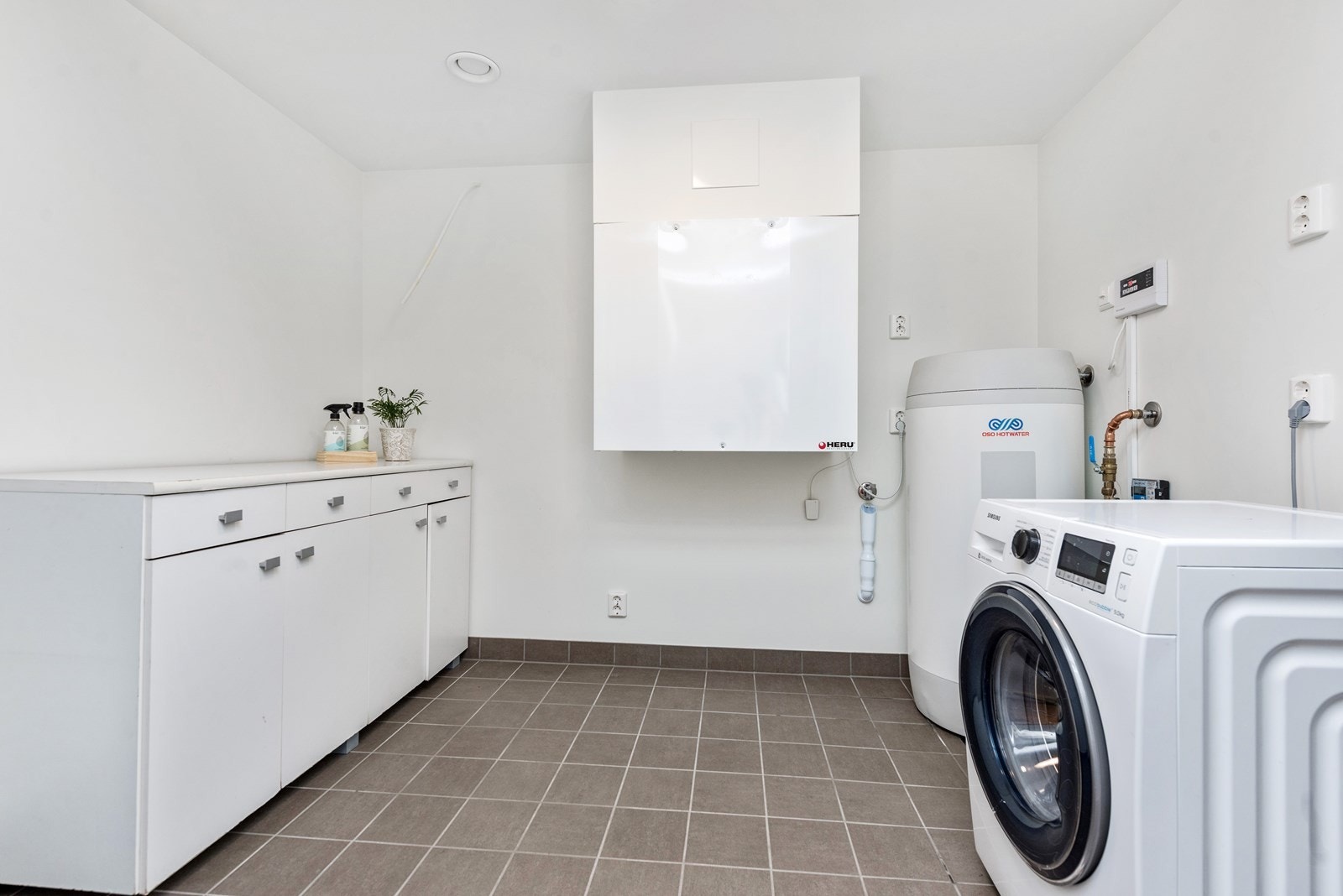 Vaskerommet har grått flisegulv med gulvvarme og hvitmalte vegger Galleribilde