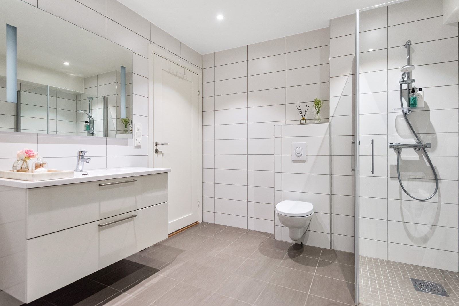 Badet har moderne servantinnredning, speil, vegghengt toalett og et dusjhjørne med glassdører Galleribilde