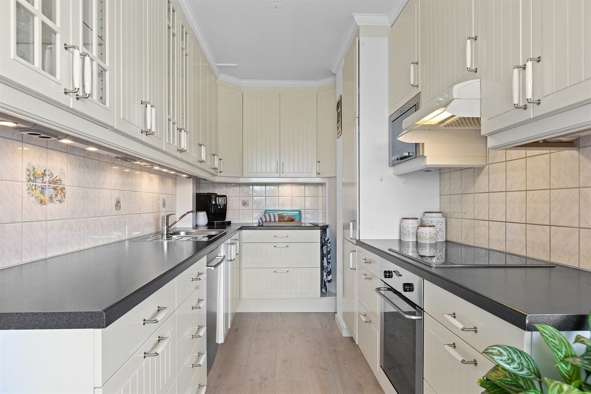 Kjøkkenet har lys og fin innredning med bl.a. fire glassdører i overskap og laminat benkeplater med nedfelt stålkum Galleribilde