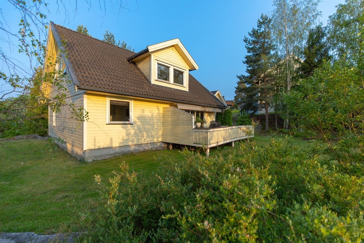 Eneboligen er omkranset av en stor hage opparbeidet med plen, busker, trær og gangsti med belegningsstein. Galleribilde