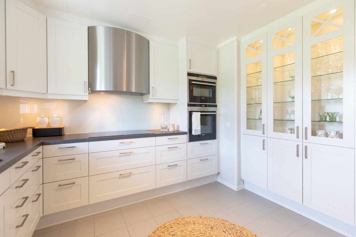 Vitrineskap med spotlights, kolonialskuffer, herdet glass mellom overskap/benk, oppvaskmaskin, innbygd fjøl, Røroshetta ventilator i børstet stål, nedfelte stekeplater med boost og induksjon, innebygd komfyr og kombinert micro/komfyr. Galleribilde