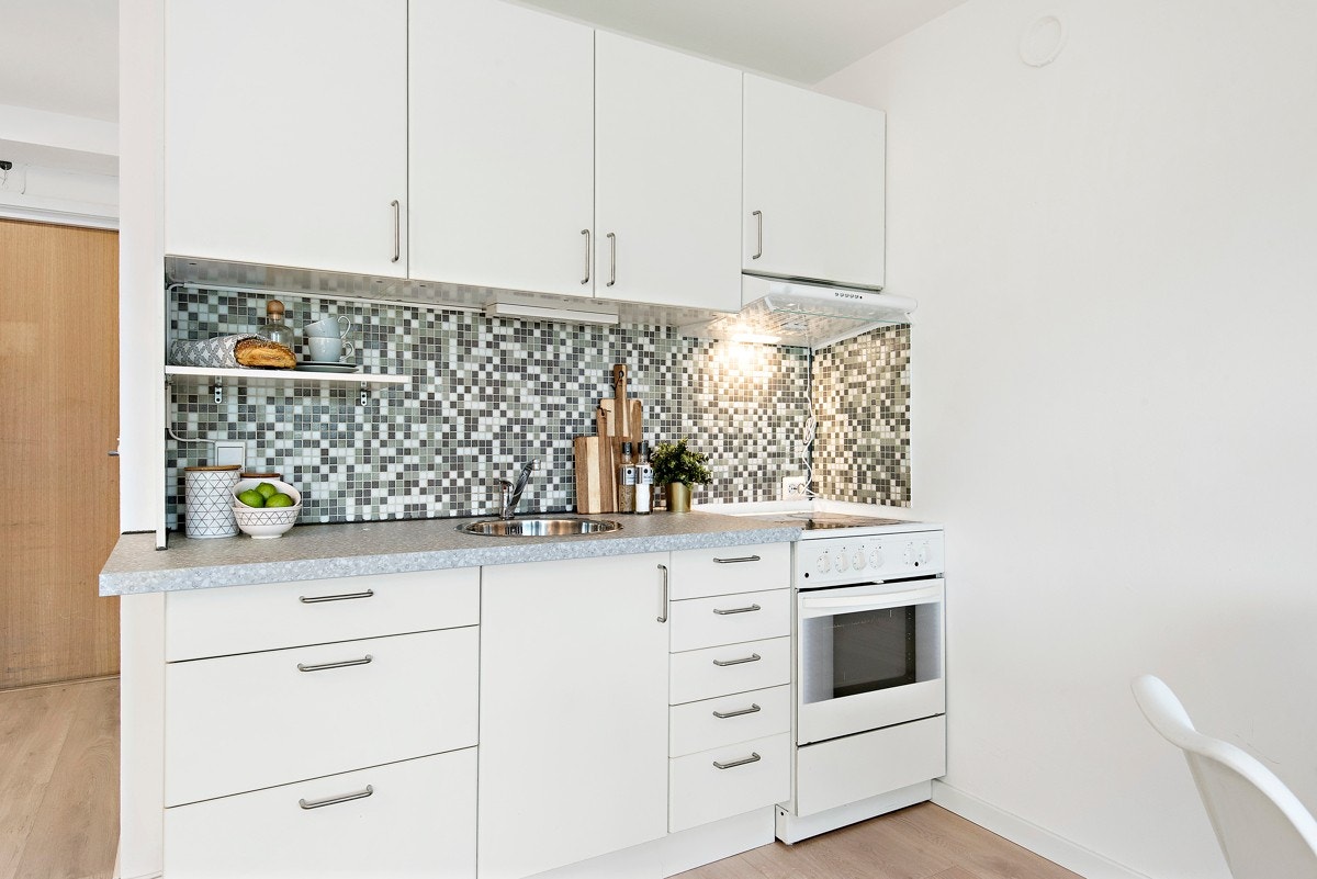 Moderne kjøkken med glatte folierte fronter og børstede stålgrep. Laminert benkeplate med glassmosaikkfliser og mye skapplass. Galleribilde